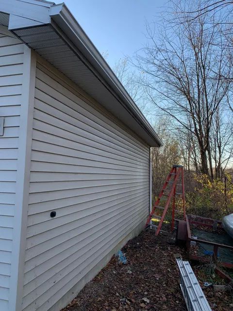 Backyard view of a house siding, ladder, bare trees, and a red metal frame under a blue sky