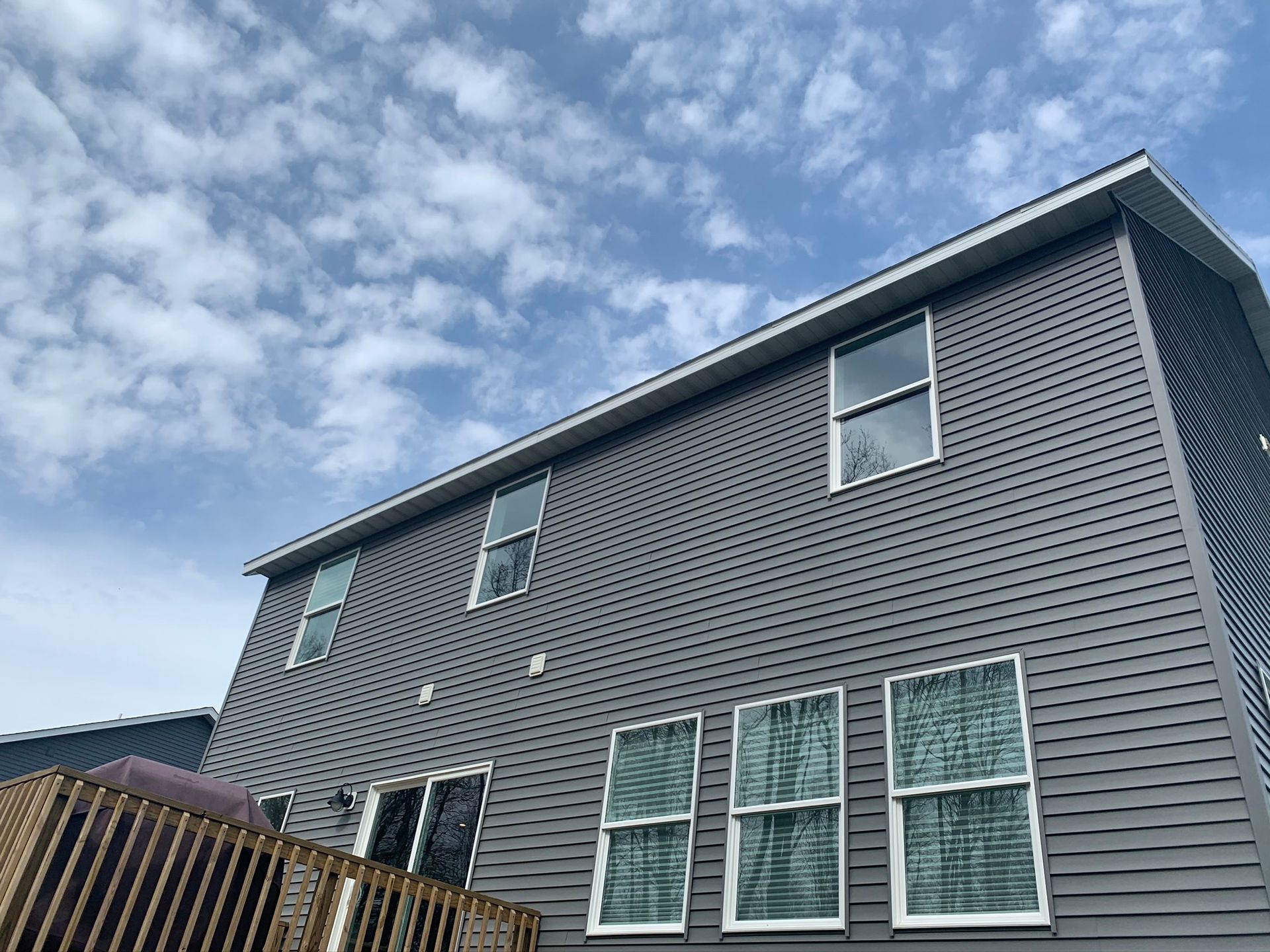 Exterior of a gray two-story house with white-trim windows under a cloudy sky