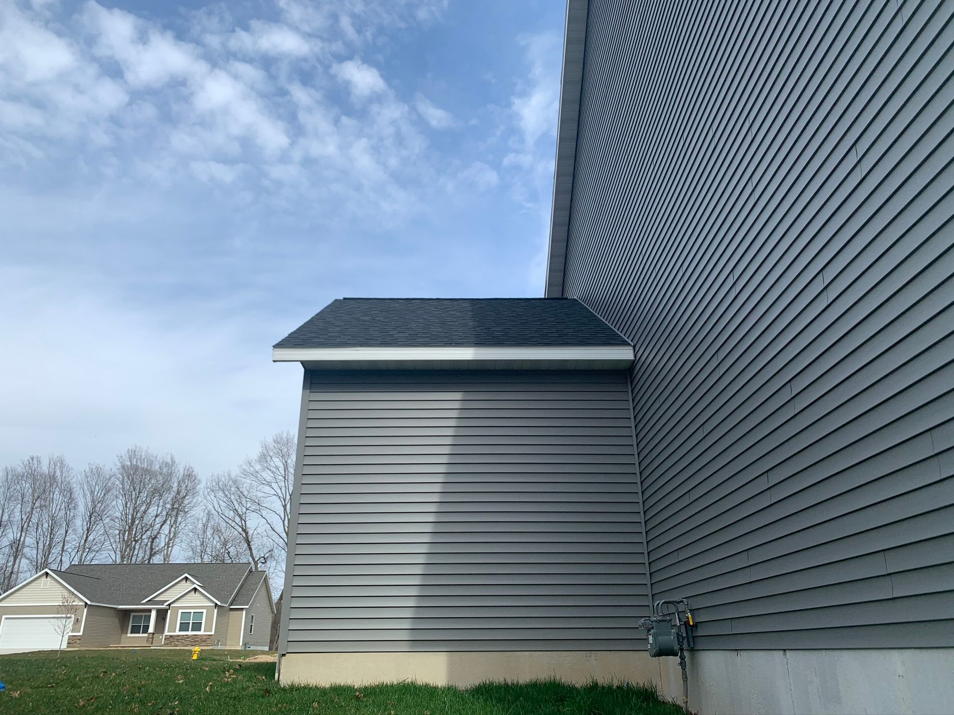 Gray vinyl-sided house exterior with a small side addition under a blue sky