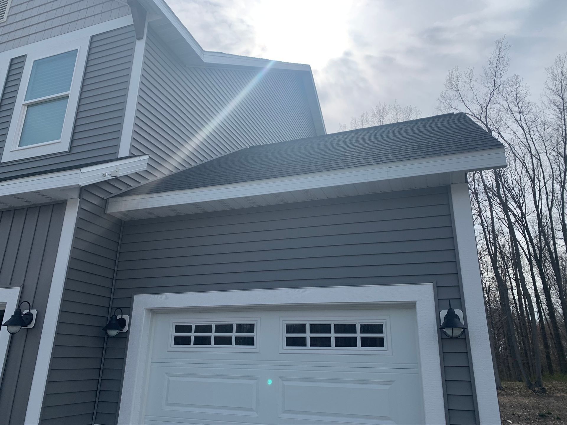 Gray house exterior with white garage door and sloped roof under a cloudy sky