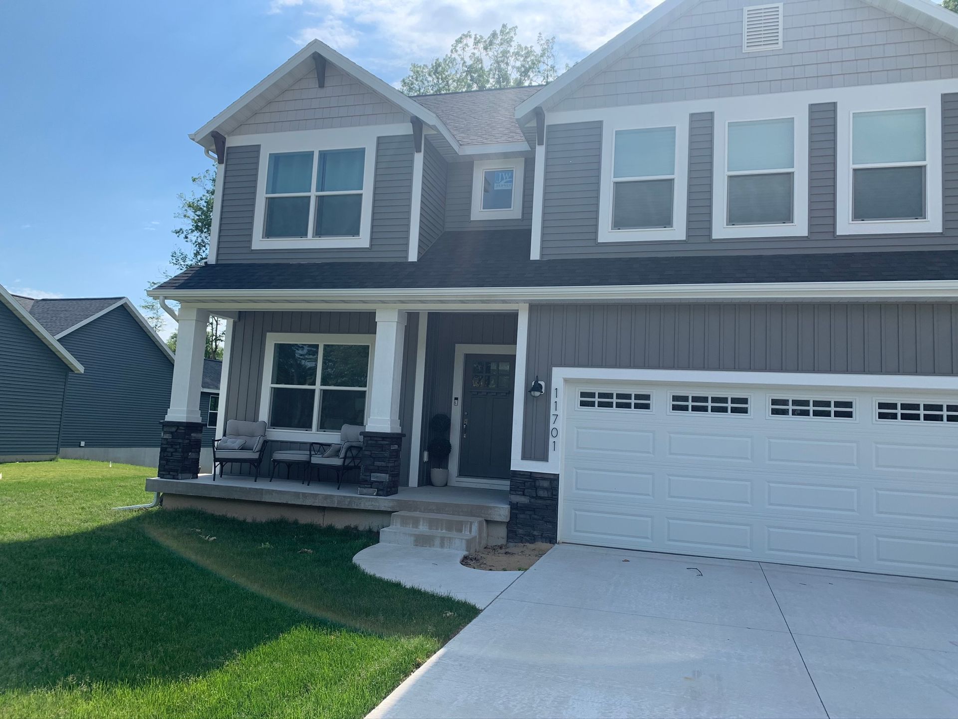 Two-story suburban house with front porch, white garage, and concrete driveway in daylight