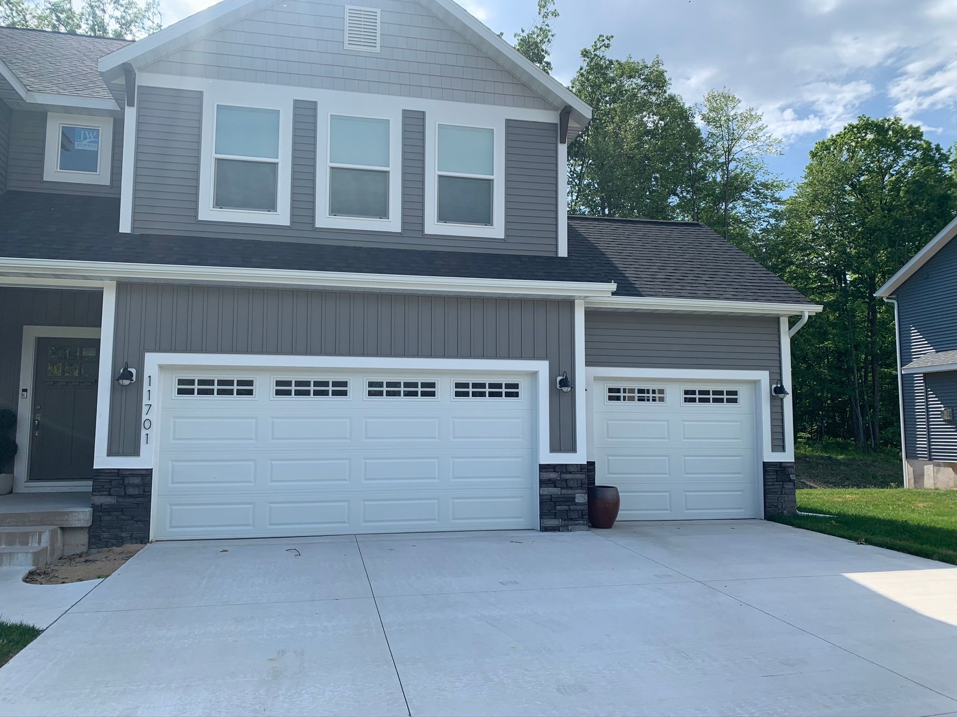 Suburban house with two white garage doors and a light gray driveway under a bright sky