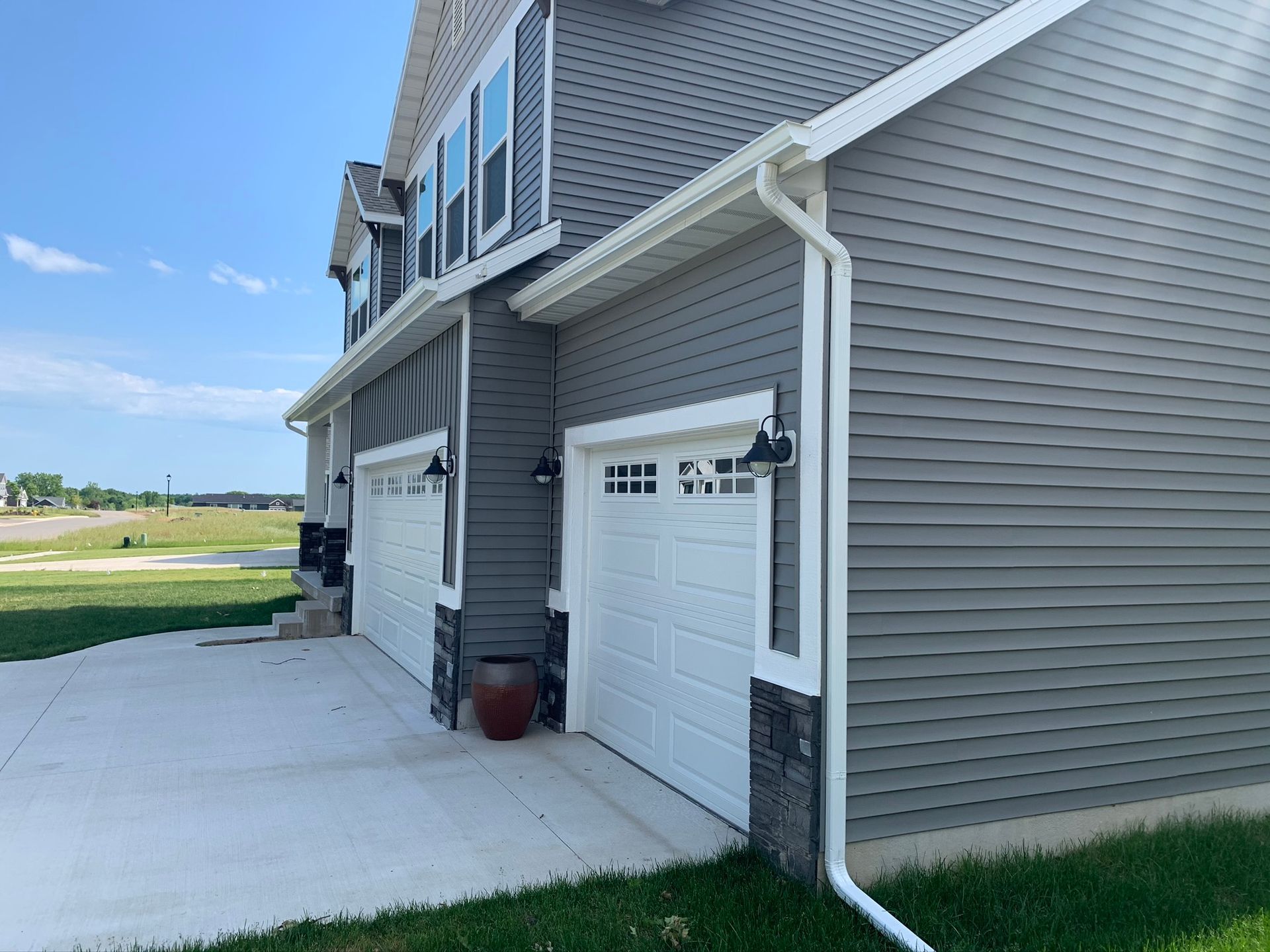 Gray house exterior with white garage doors and a concrete driveway beside a grassy field.