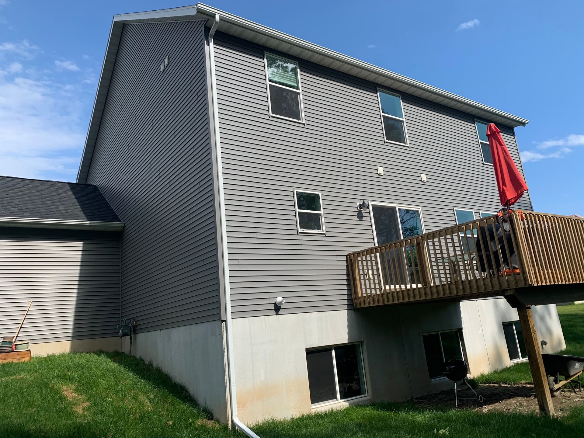 Gray house with white trim and a wooden deck under a blue sky