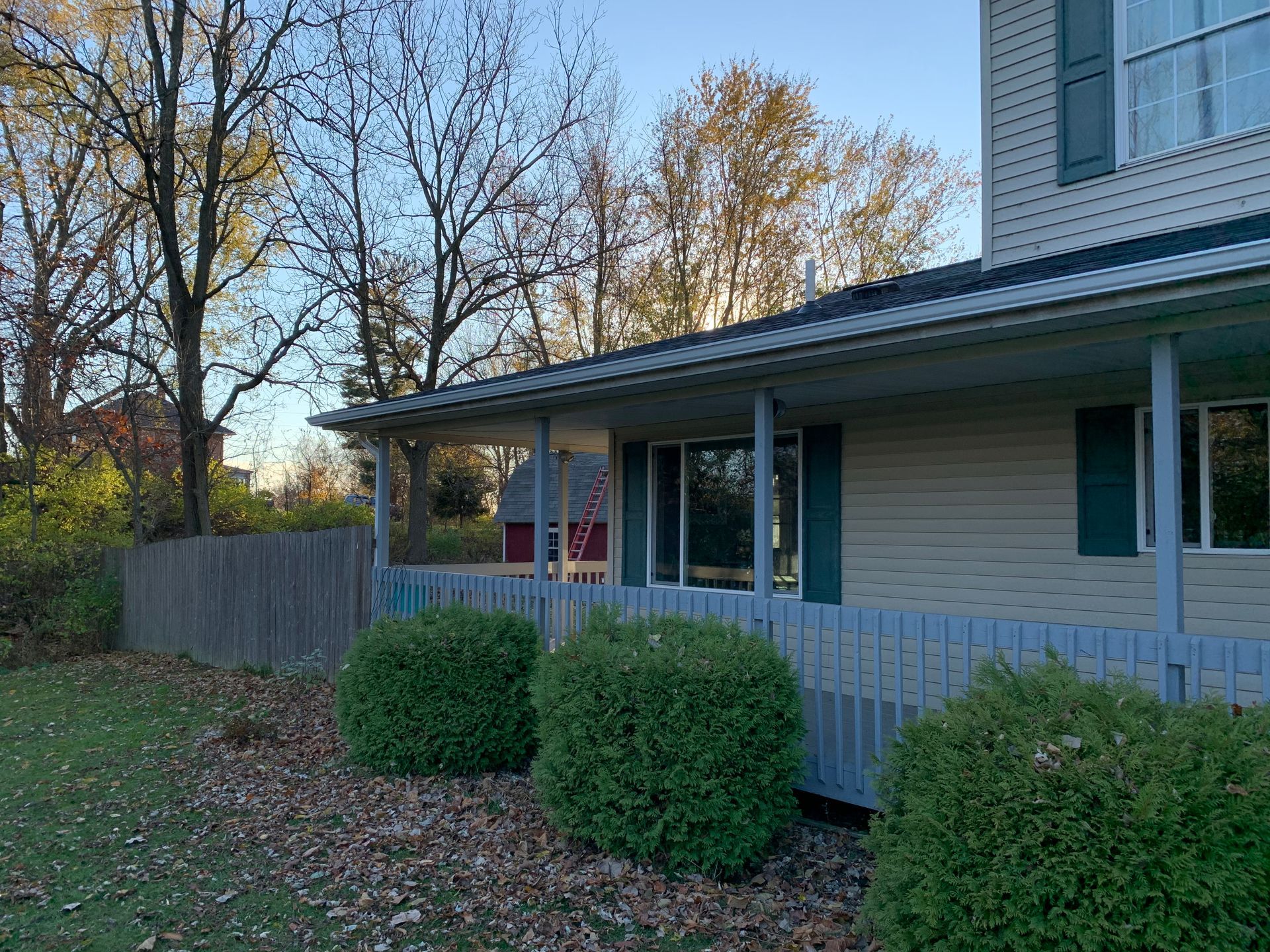 Suburban house with a covered porch, leaf-covered yard, and trimmed bushes in the foreground