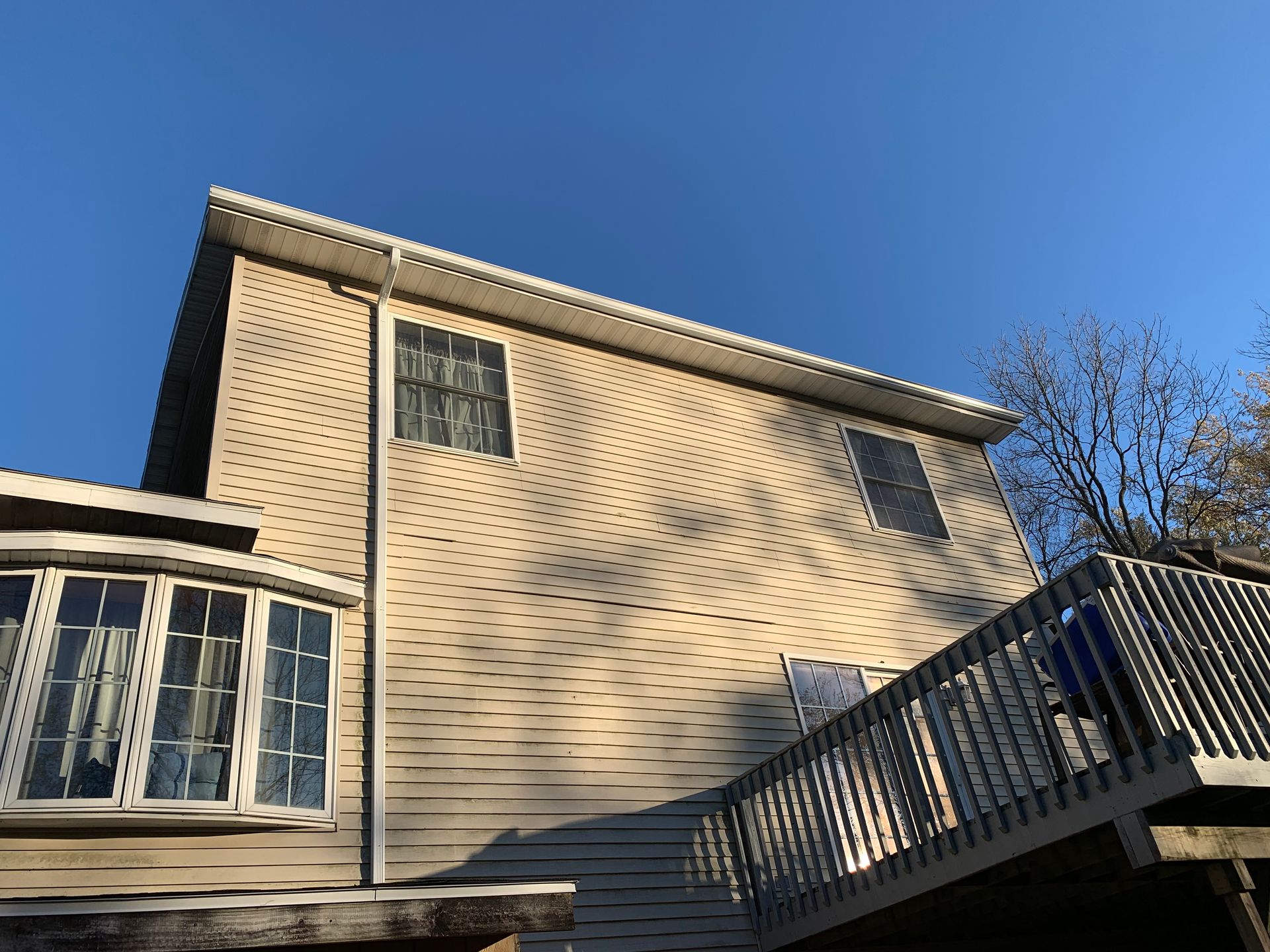 Exterior of a beige house with windows and a wooden deck under a clear blue sky