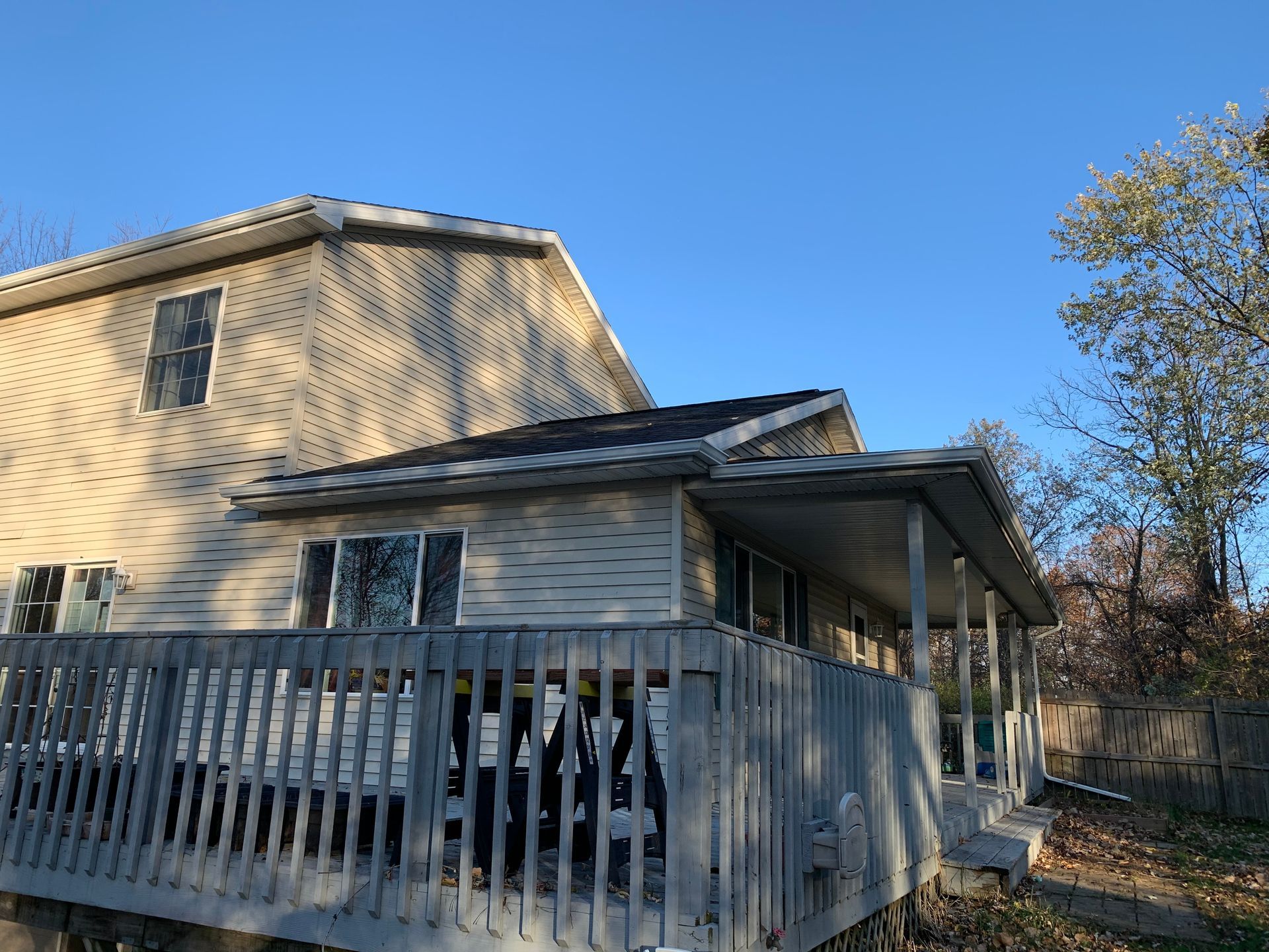 Two-story beige house with a white deck railing under a blue sky