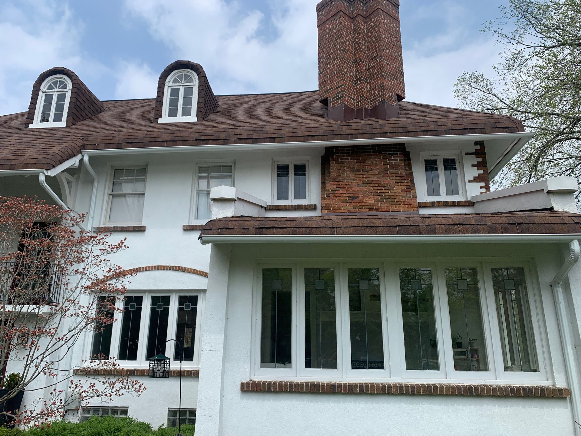 White house with brick chimney, dormer windows, and a screened porch under a cloudy sky