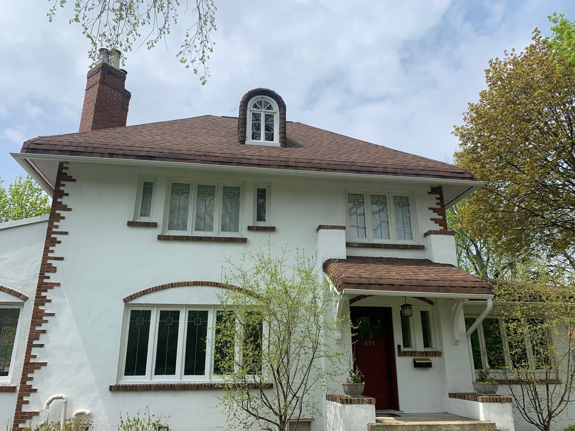 White two-story house with brown roof, red front door, and trees in front