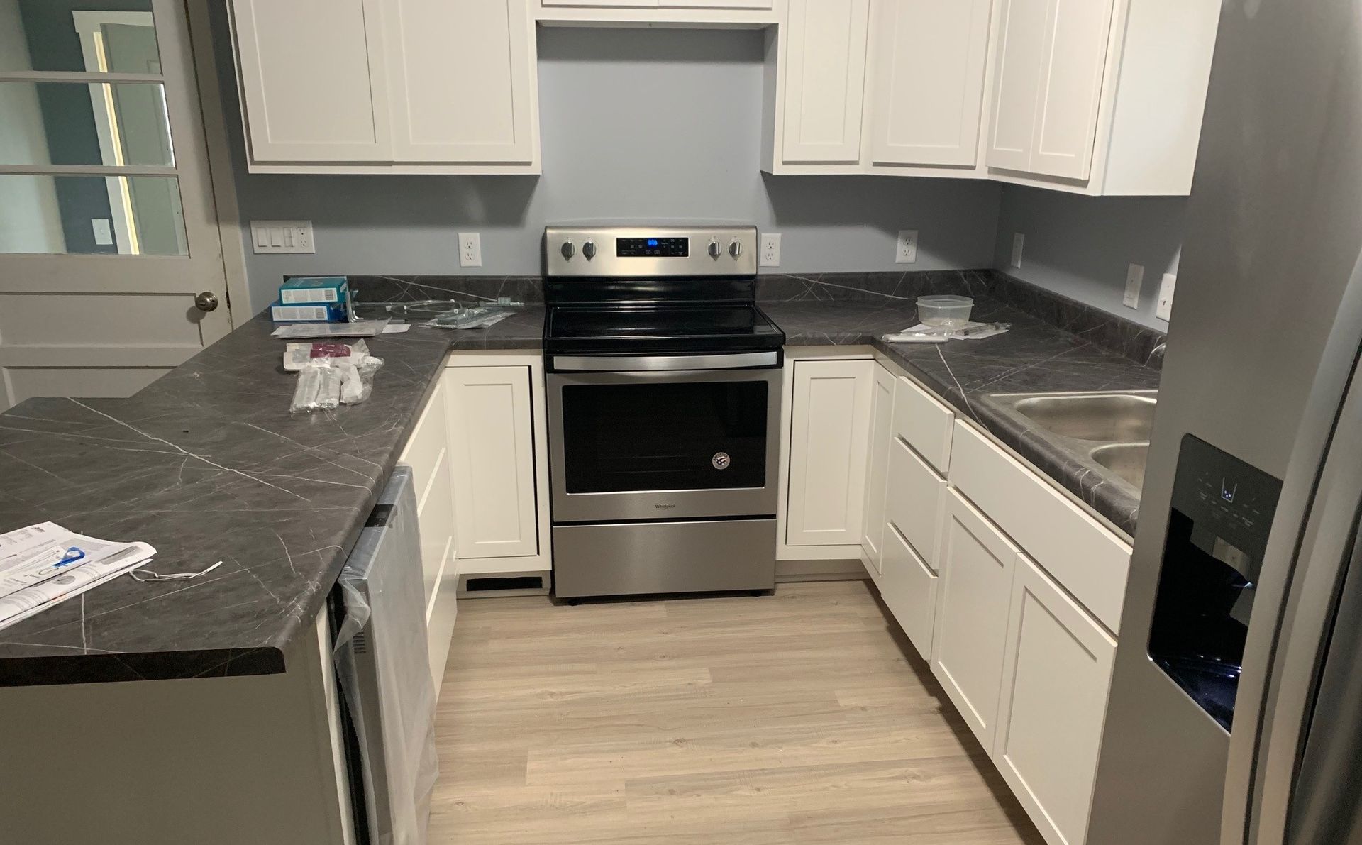 Modern kitchen with dark countertops, white cabinets, stainless steel oven, and light wood floor
