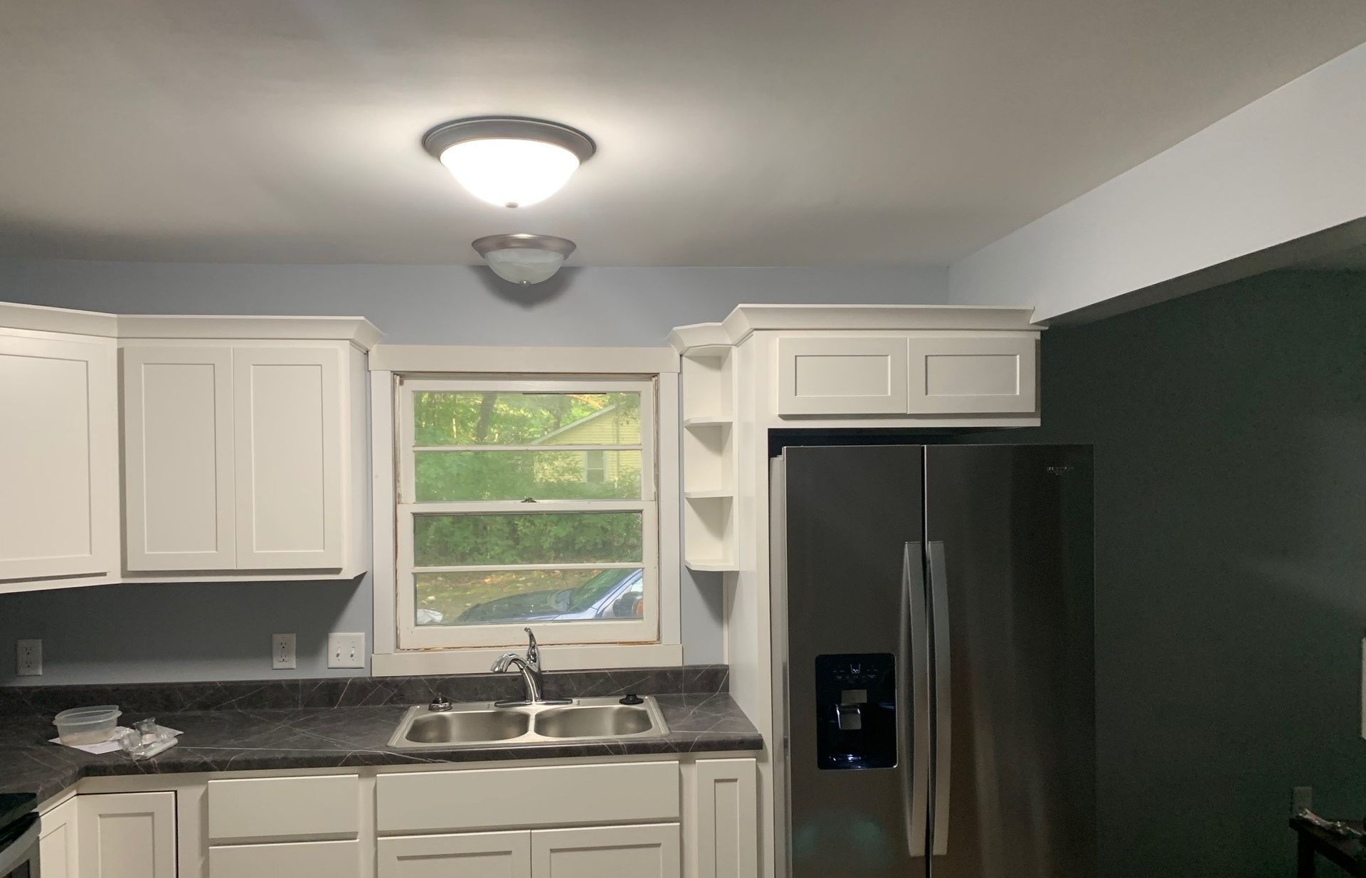 Small kitchen with white cabinets, dark countertops, stainless fridge, and a window over the sink.