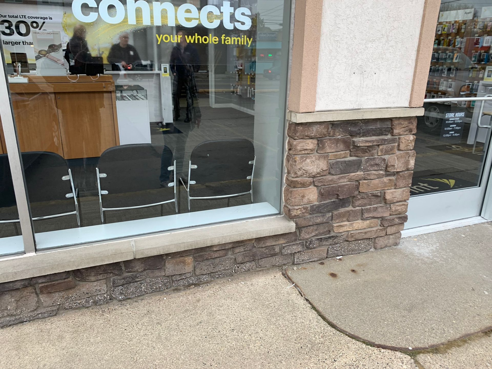 Storefront window with “Connects” sign, stone facade, and sidewalk ramp outside.