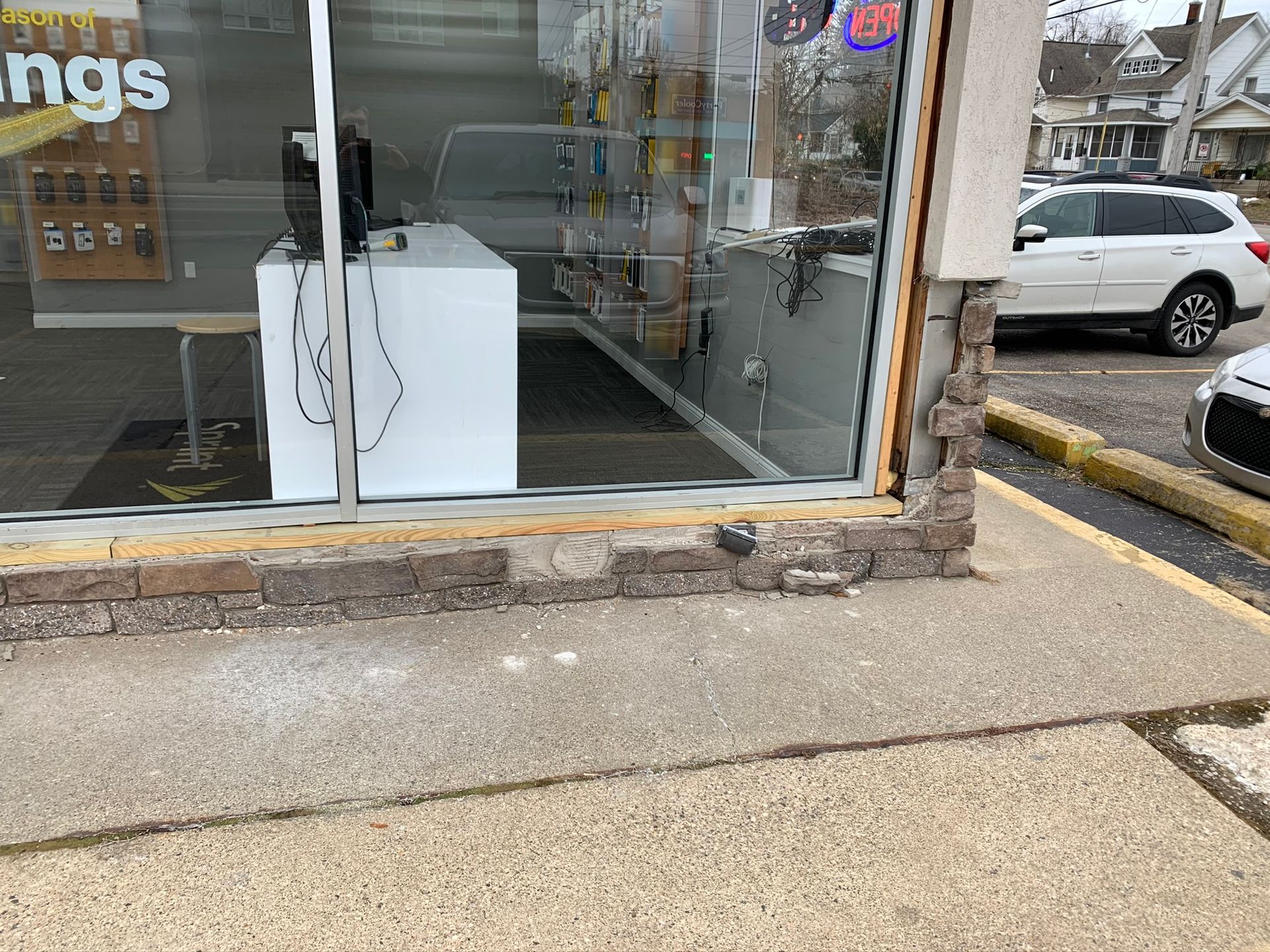Storefront entrance with large glass windows and a sidewalk curb ramp beside parked cars