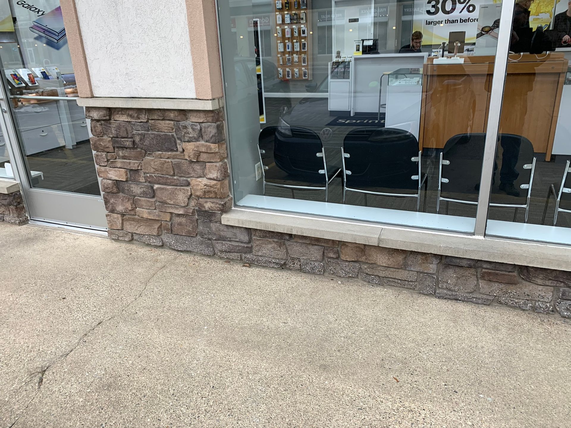 Storefront with large windows, stone base, and empty paved walkway outside.