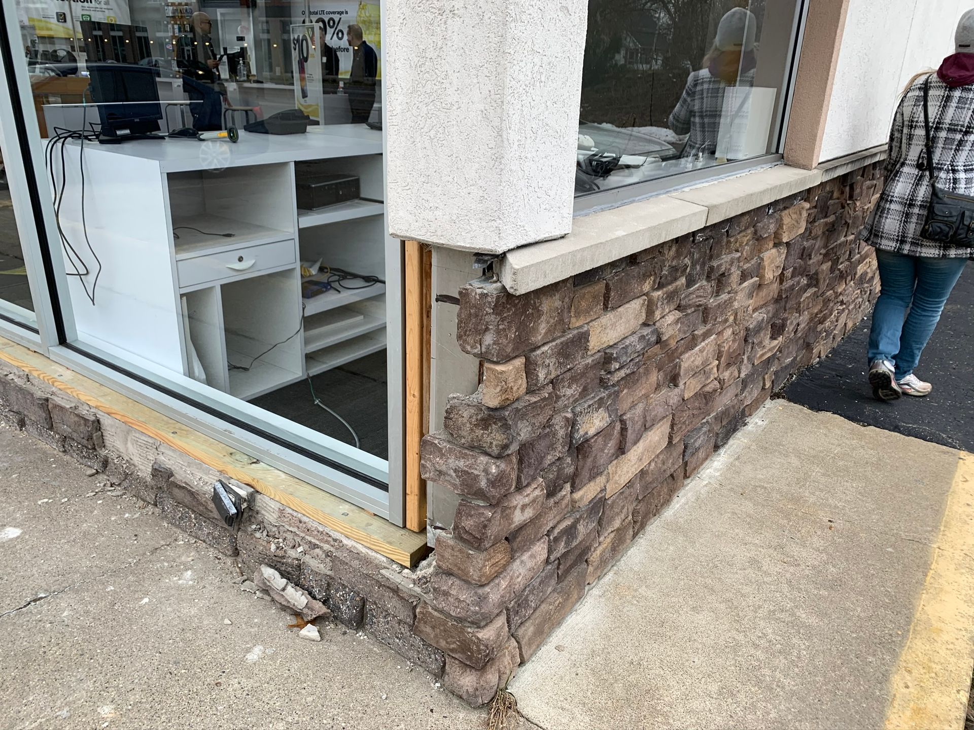 Storefront corner with cracked stone base, window display, and a person walking on the sidewalk