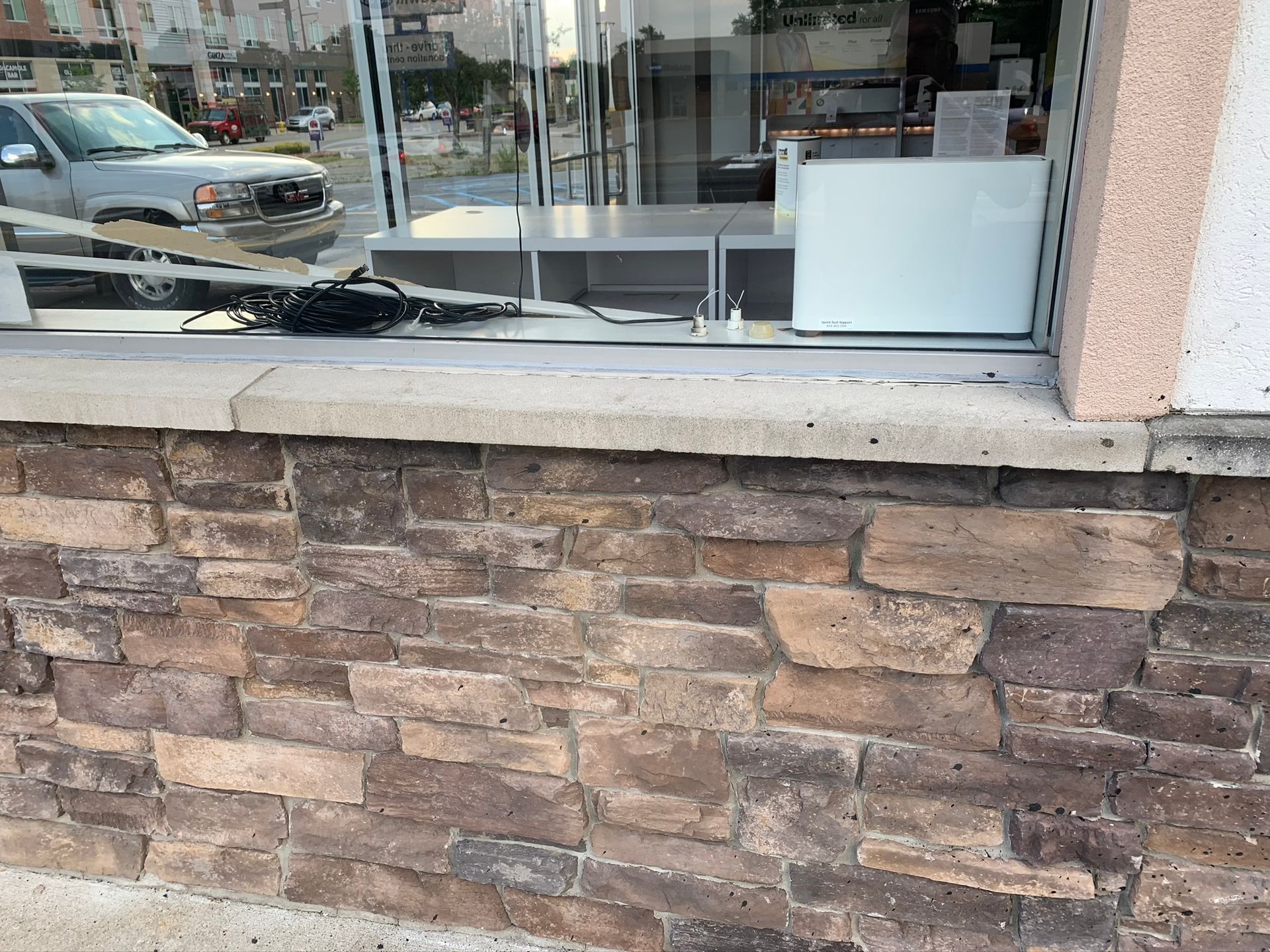 Storefront window above a stone-faced wall with a white sign inside and a street reflection in the glass
