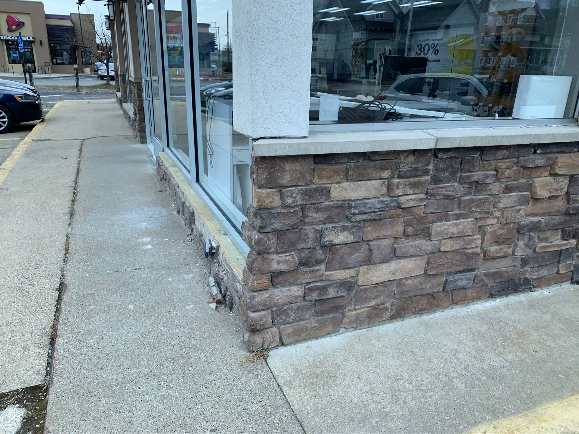 Sidewalk beside a storefront with stone facade and large windows on a city street