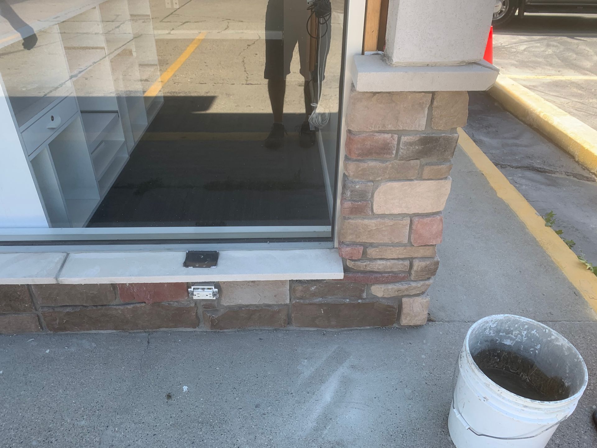 Storefront glass door with brick wall and a white bucket on the sidewalk