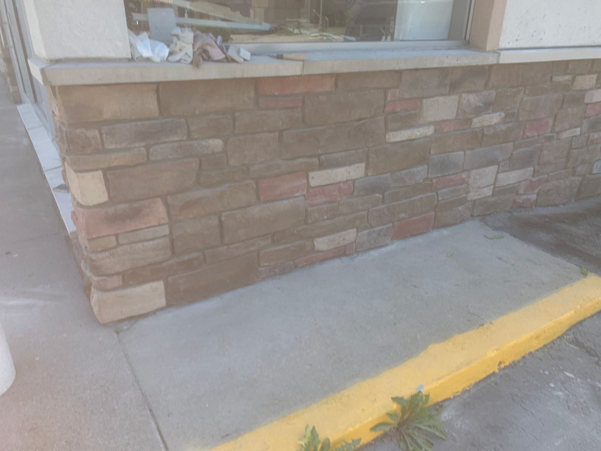 Stone-faced storefront corner with a concrete sidewalk and yellow curb ramp line