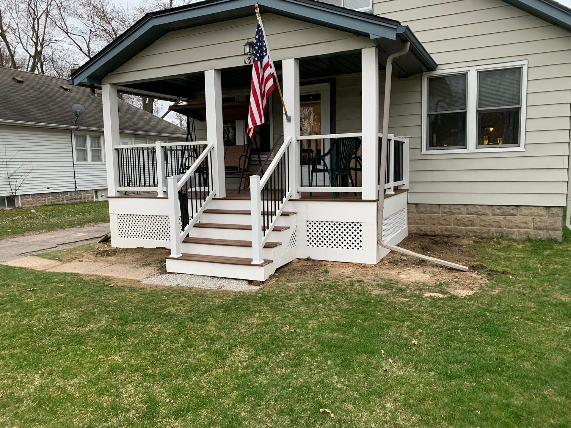 Front porch with steps, white railings, and an American flag on a beige house