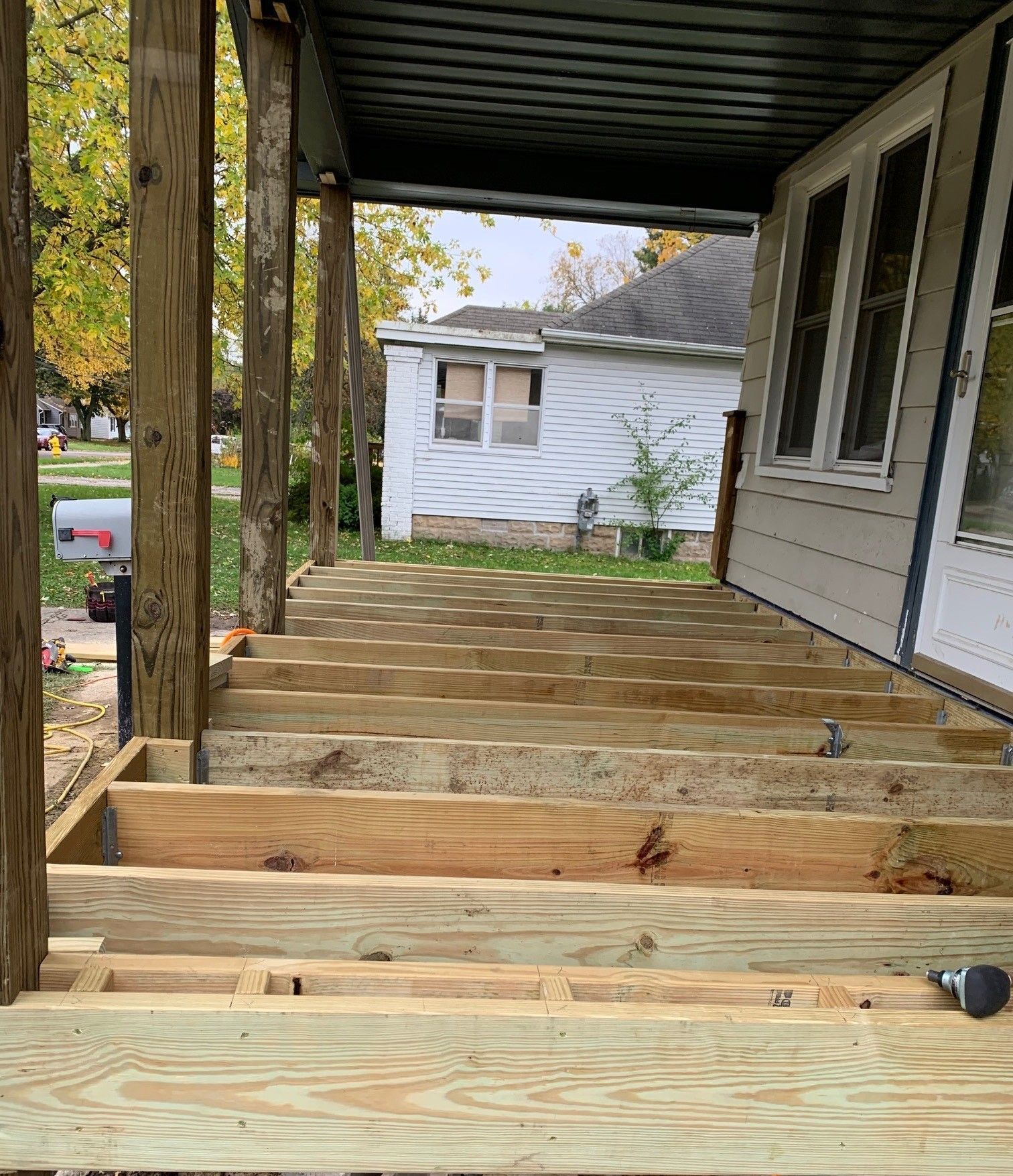 Partially built wooden porch deck beside a white house, viewed from the steps under a covered roof