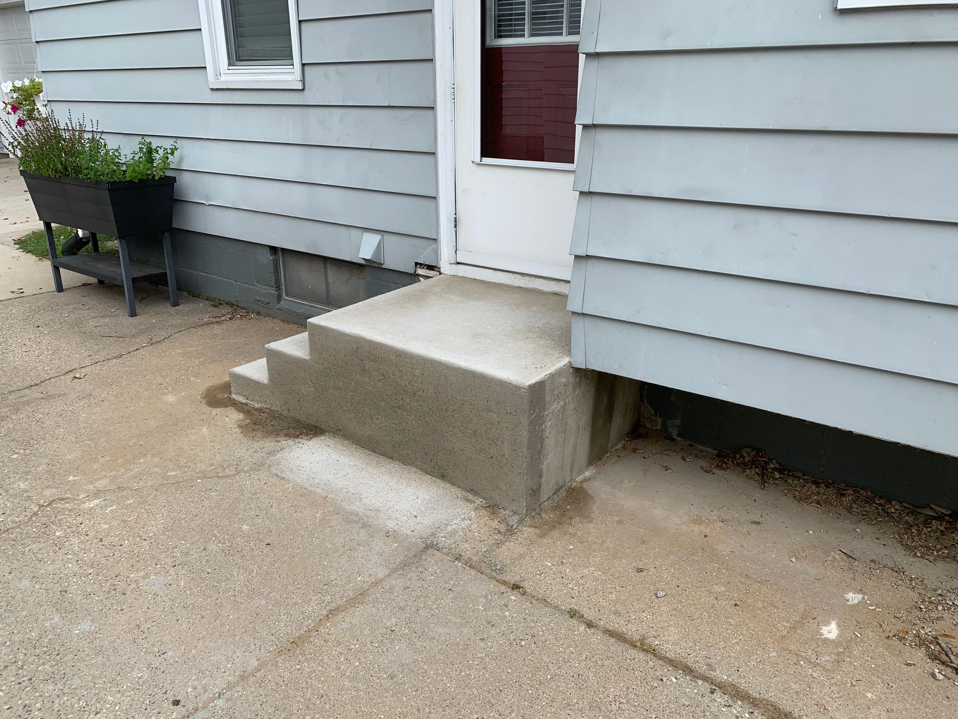 Small concrete step at a house entrance with a white door and gray siding