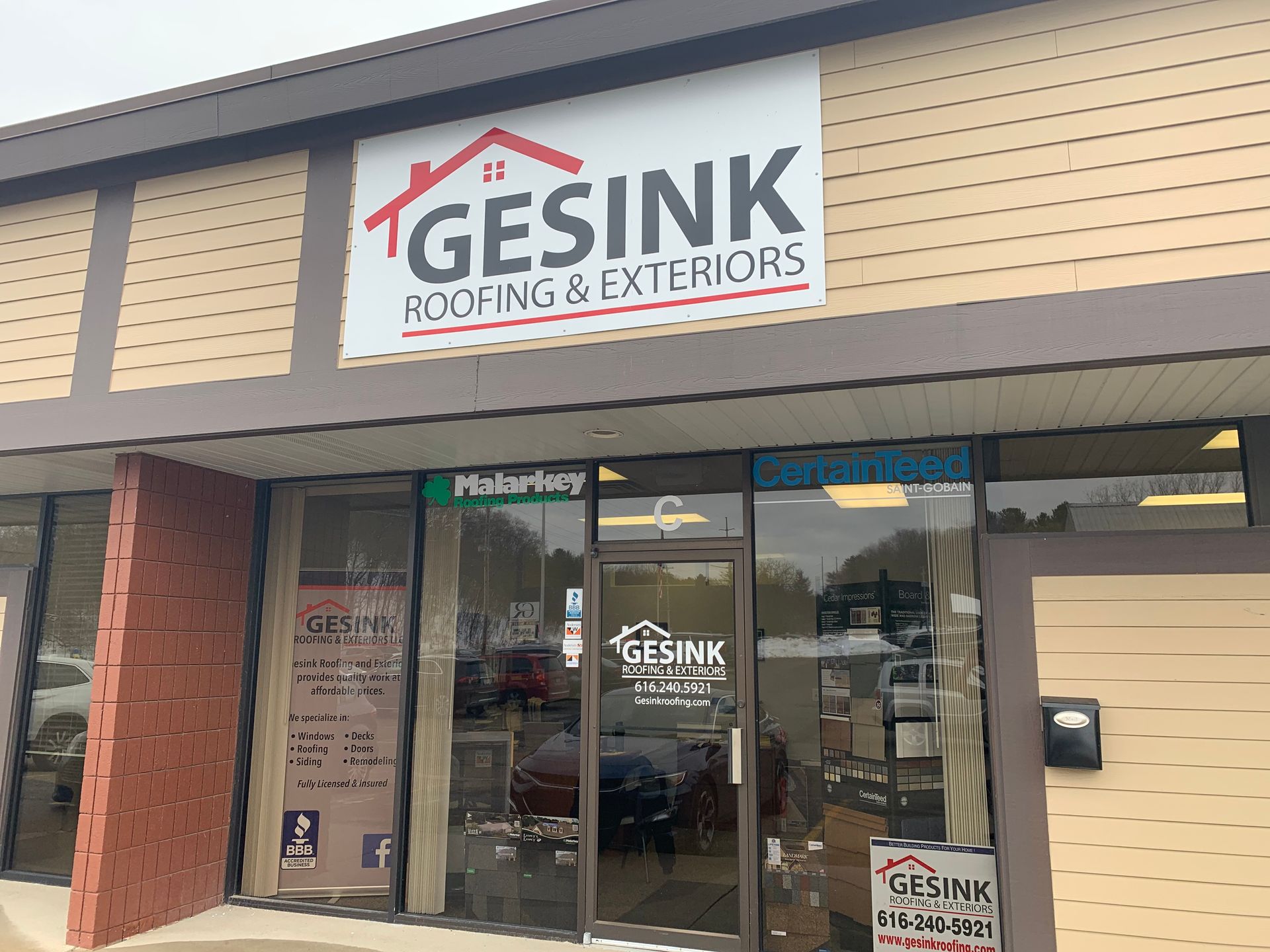Storefront of Gesink Roofing & Exteriors with glass doors and tan siding on a commercial building.
