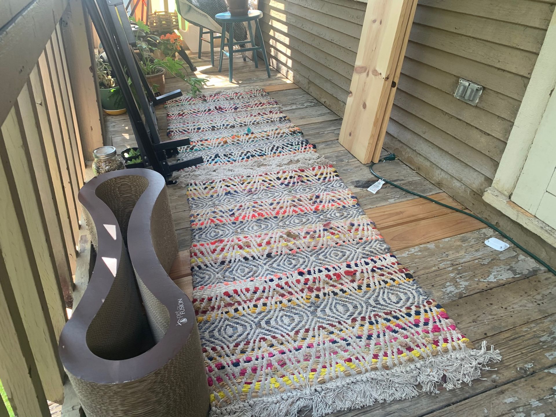 Colorful striped rug runner on a narrow outdoor walkway beside tan siding and a planter.