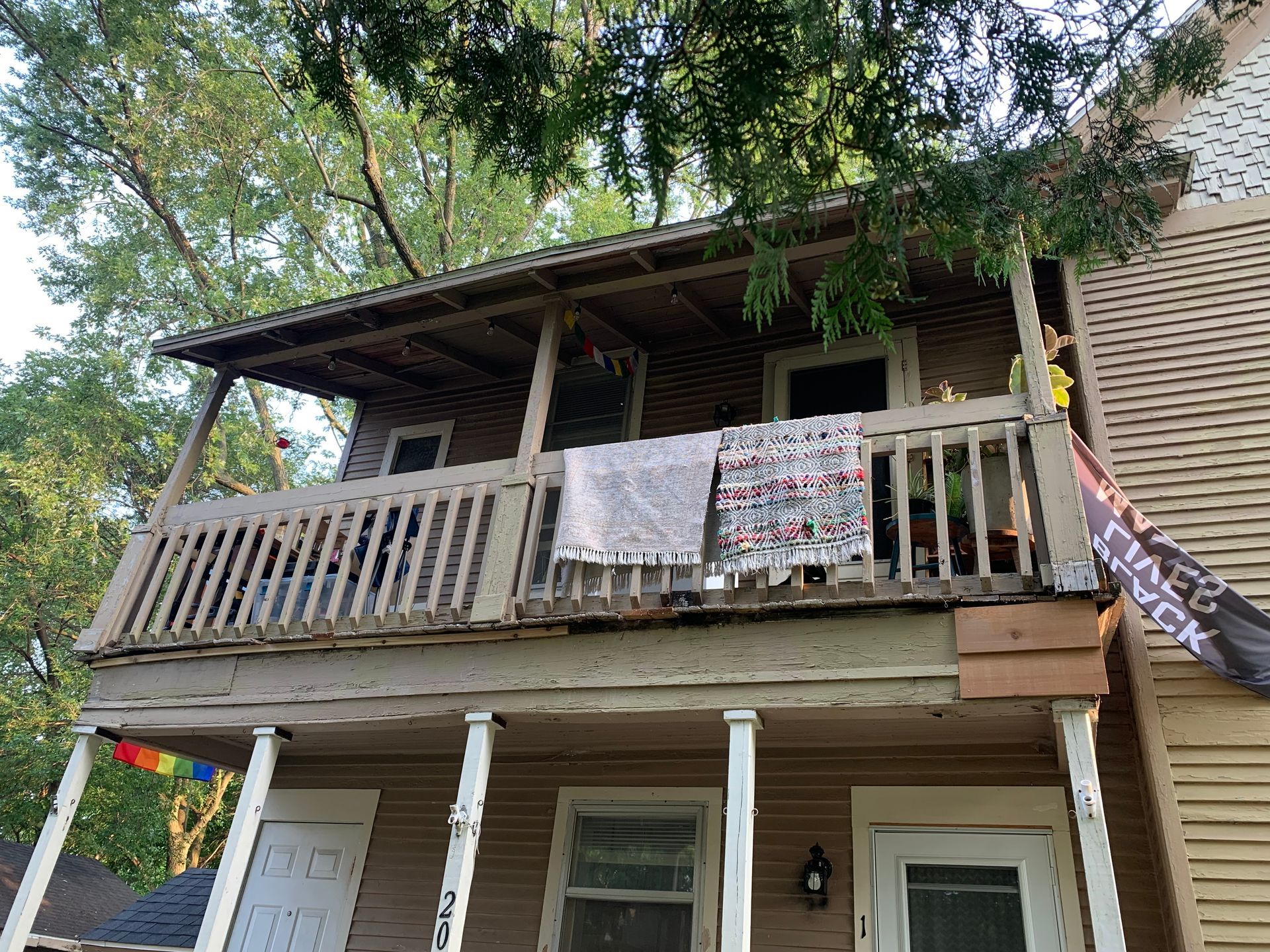 Two-story house with a covered balcony and hanging laundry under trees