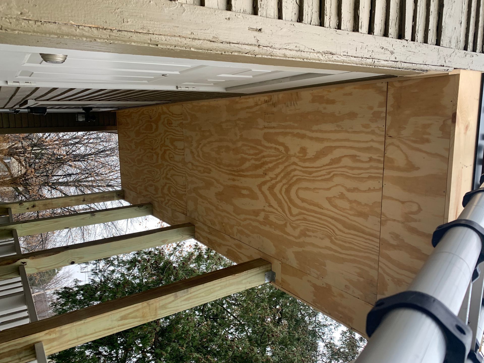 Wooden deck under construction with plywood sheathing and support beams beside trees
