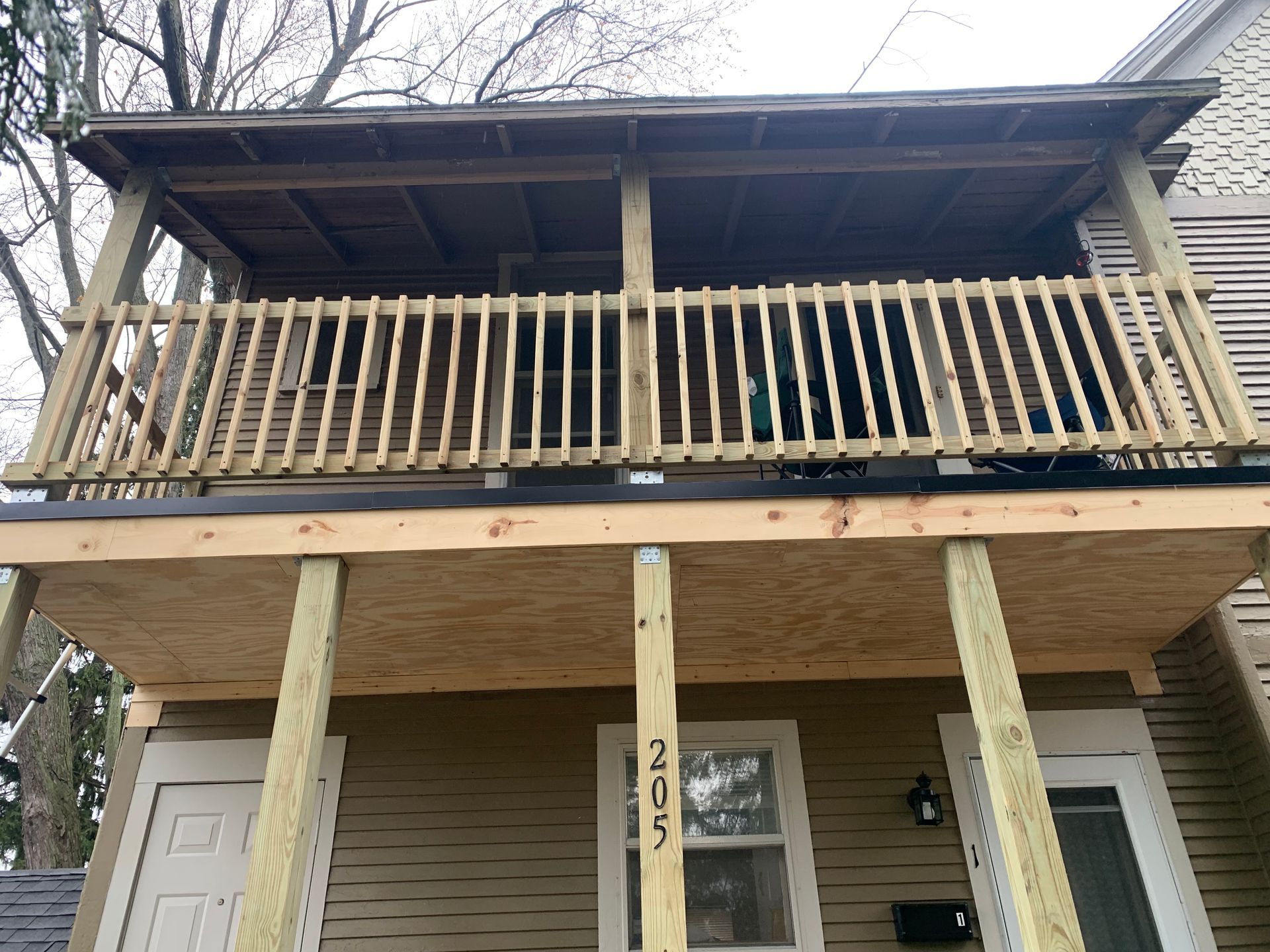 Two-story house with a front porch, wooden railing, and exposed support posts under renovation