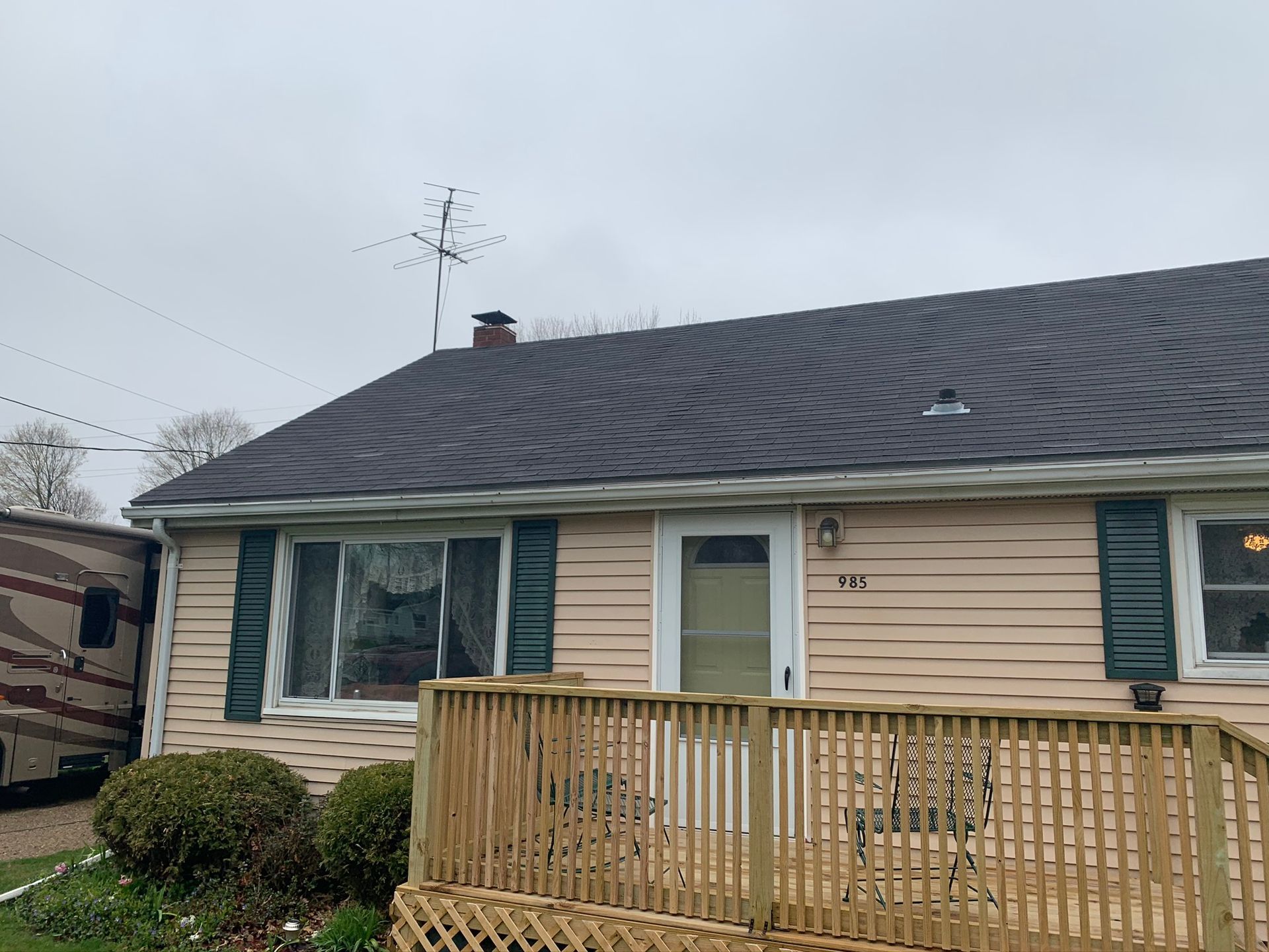 Small beige house with gray roof and front wooden deck on an overcast day