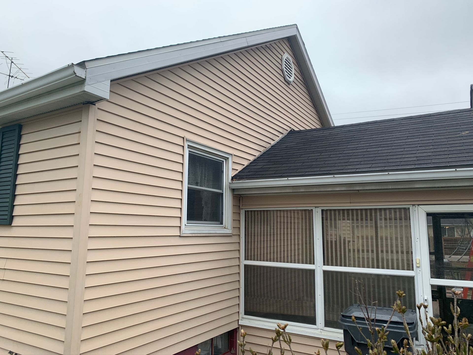 Tan vinyl-sided house exterior with a gray roof and screened porch on an overcast day