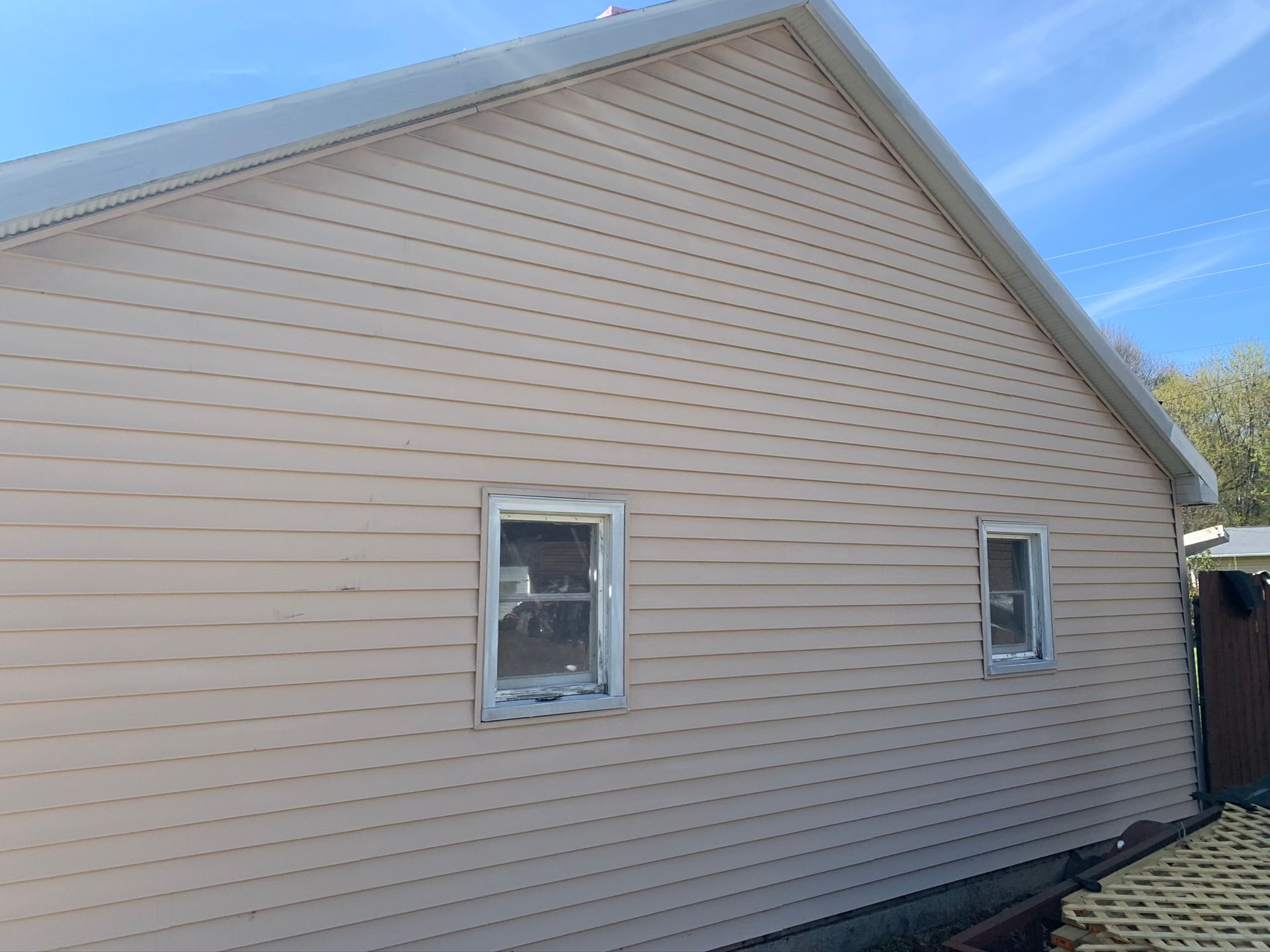 Beige house exterior with two windows, seen from the side under a blue sky.