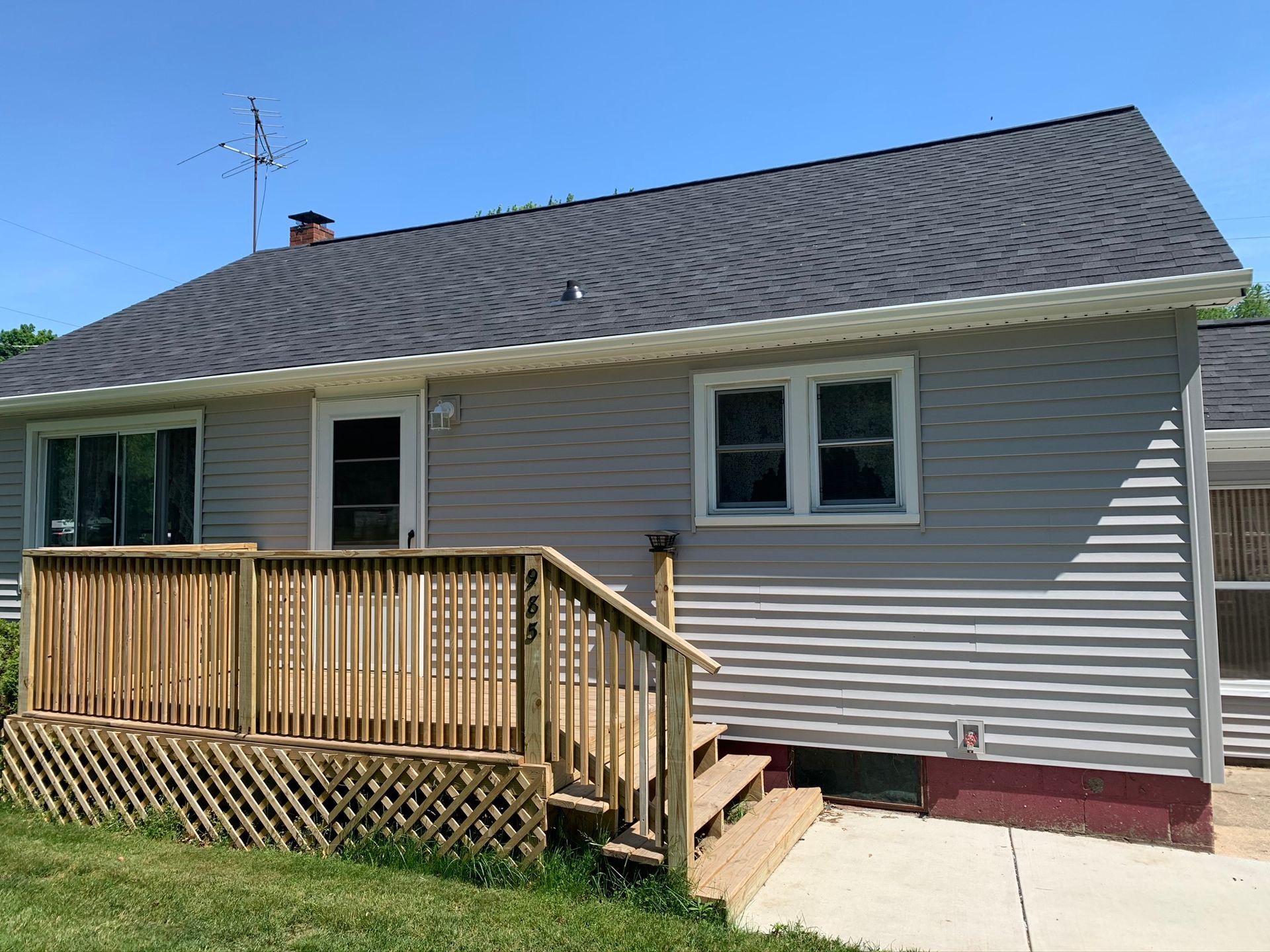 Single-story gray house with a wooden front porch and steps under a clear blue sky