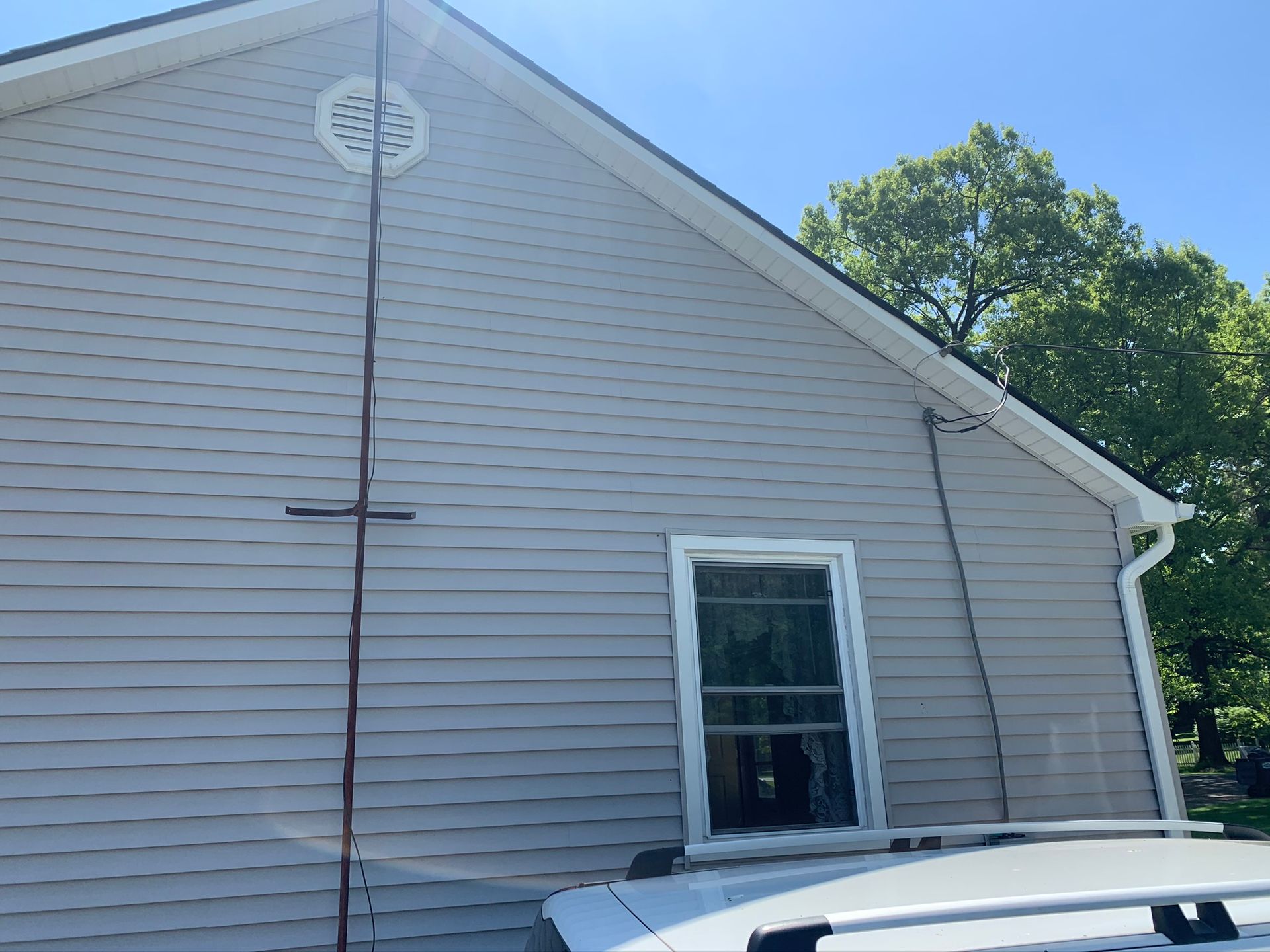 Side of a gray house with a roof vent, window, and a black cable running down the siding.
