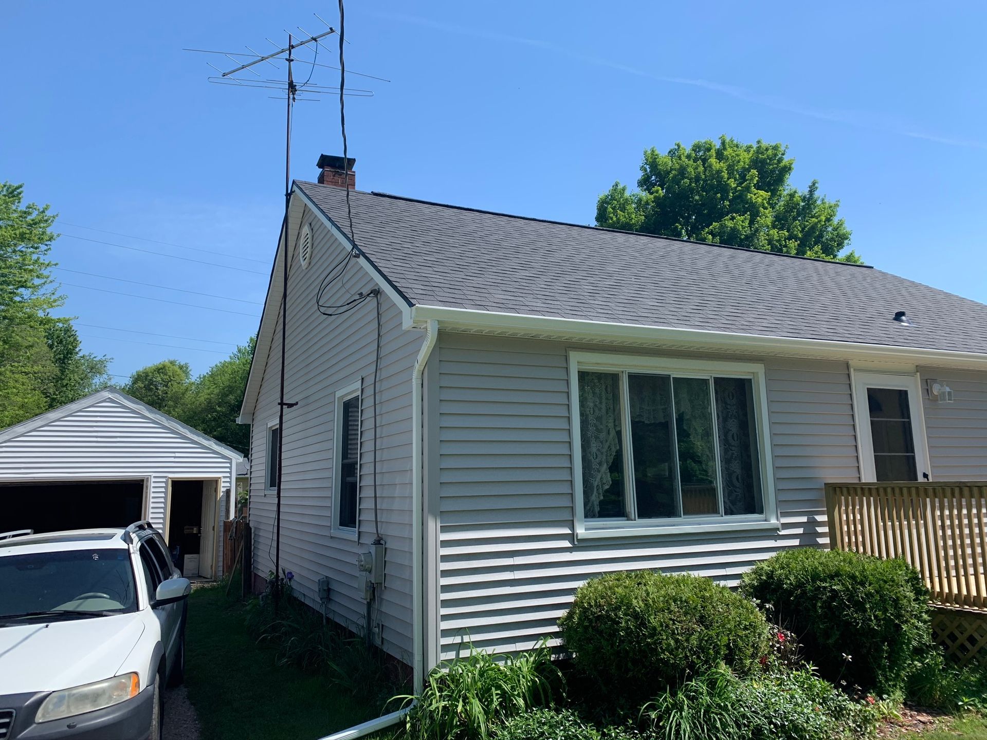 White house with gray siding and detached garage, seen from the side on a sunny day.