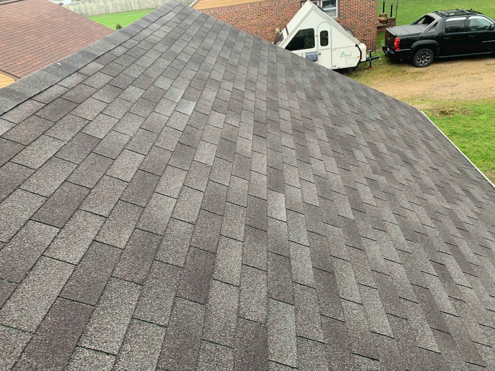 Gray shingled roof seen from above, with a small yard and vehicles in the background