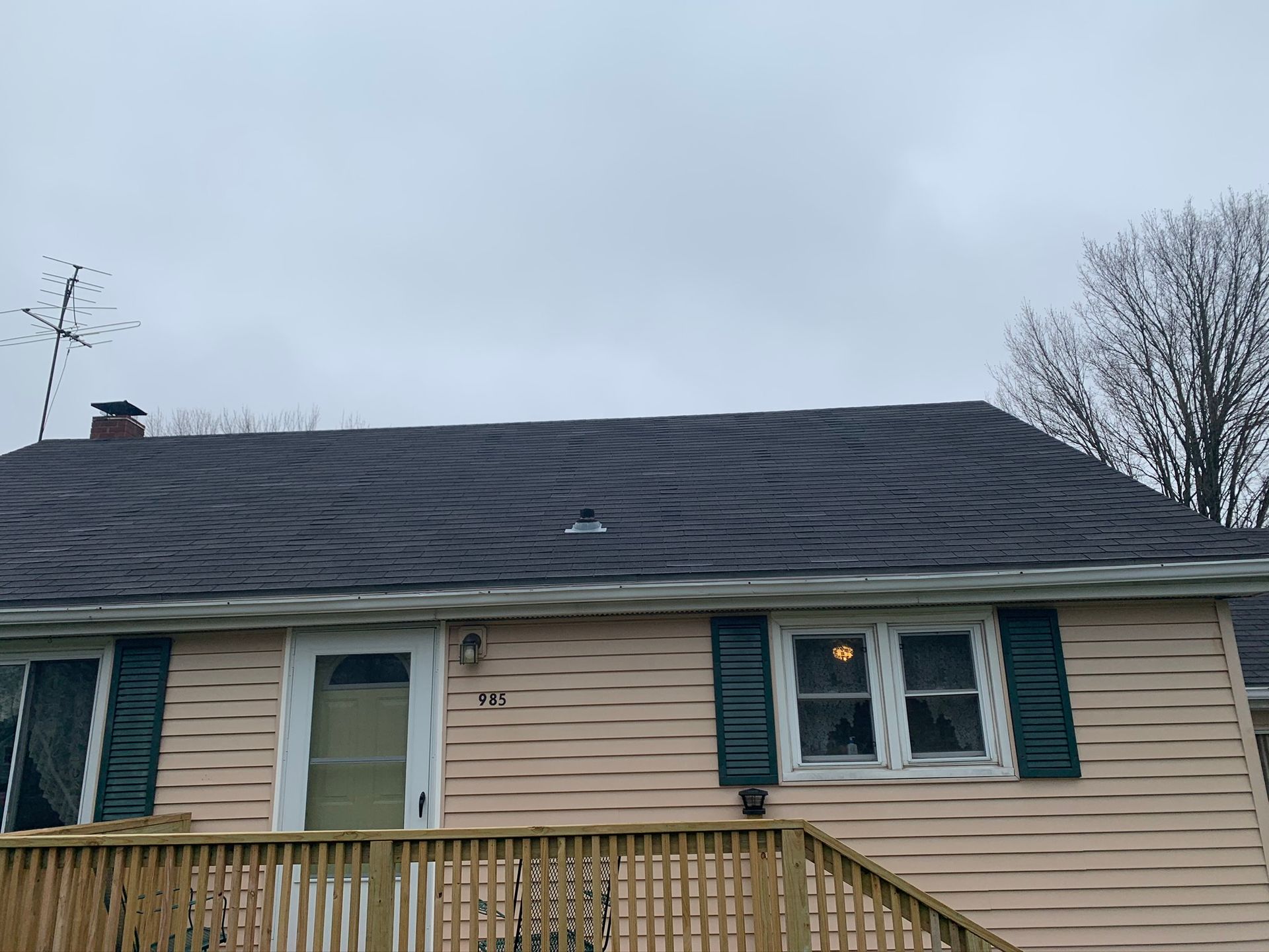 House with dark shingled roof, beige siding, teal shutters, and a wooden porch under a cloudy sky