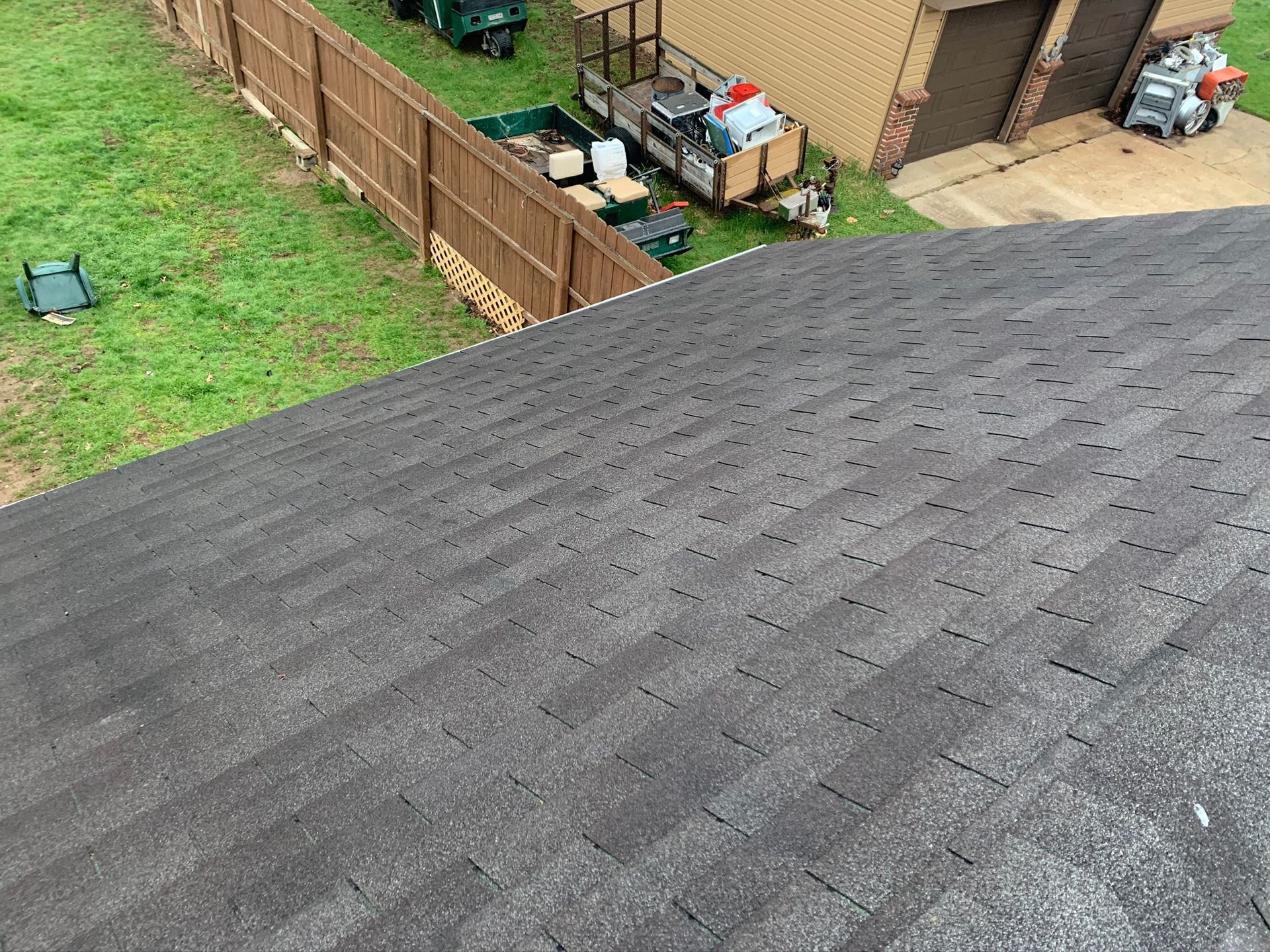 View from a roof over a fenced backyard with grass, bins, and a shed near a house