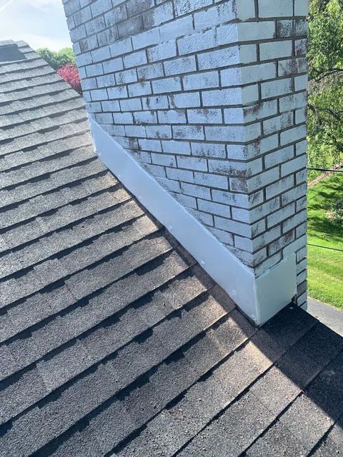 A rooftop chimney with gray shingles and light blue brick siding
