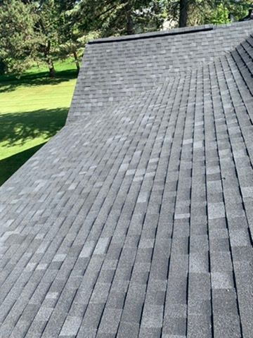 Gray shingle roof with a sloping edge beside green trees and lawn