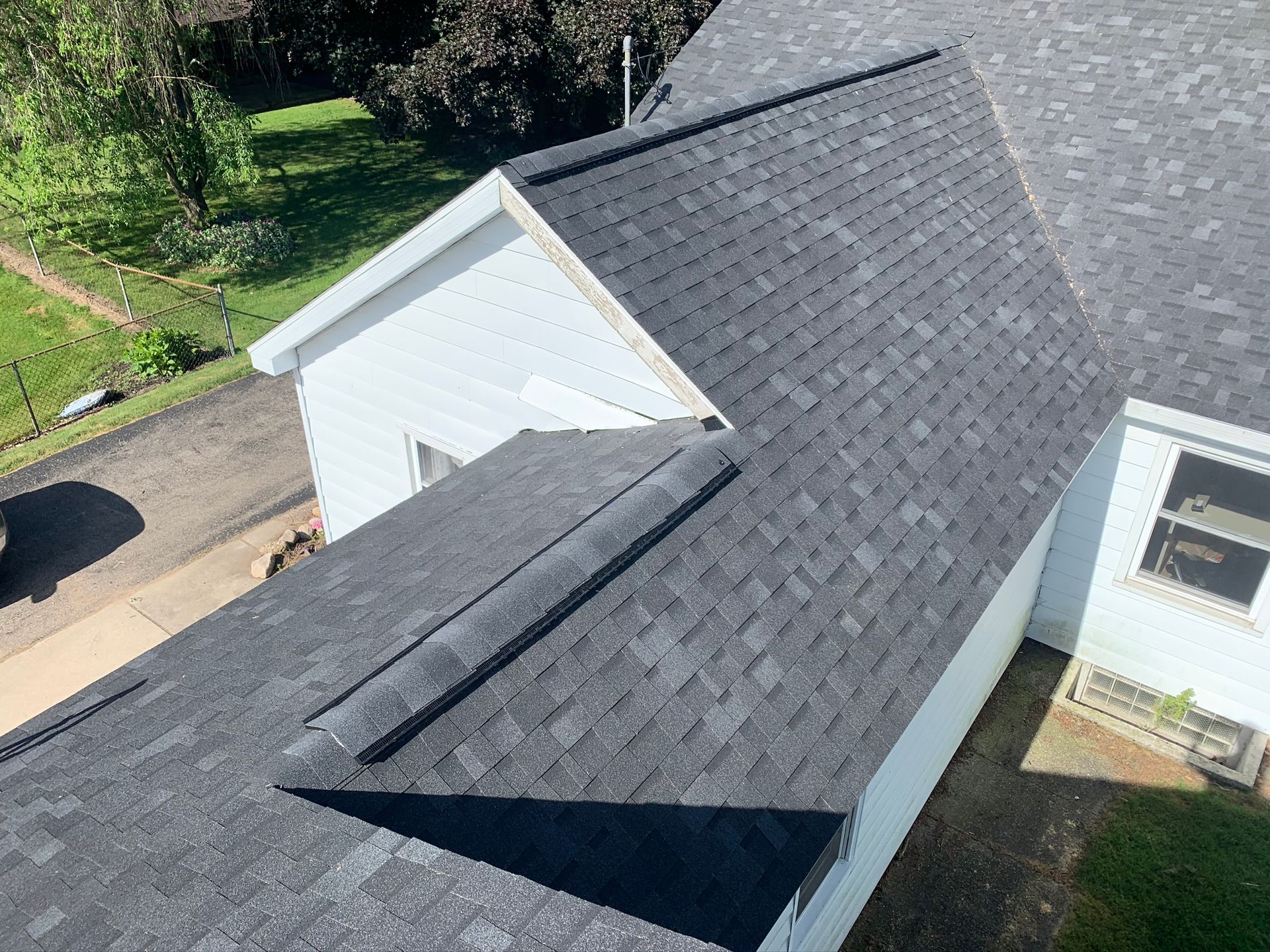 Aerial view of a house roof with dark shingles and a white siding exterior beside a driveway.