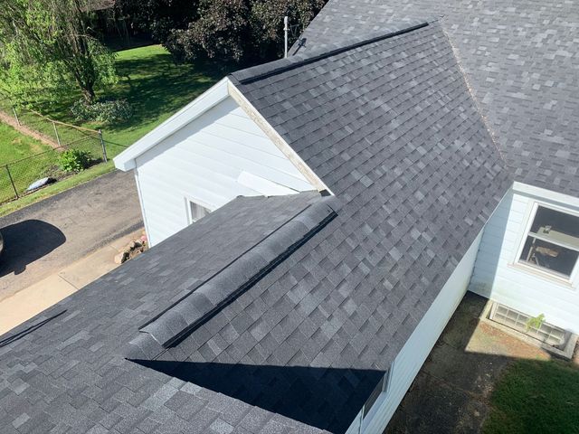 Aerial view of a gray shingled house roof with a dormer and nearby driveway.