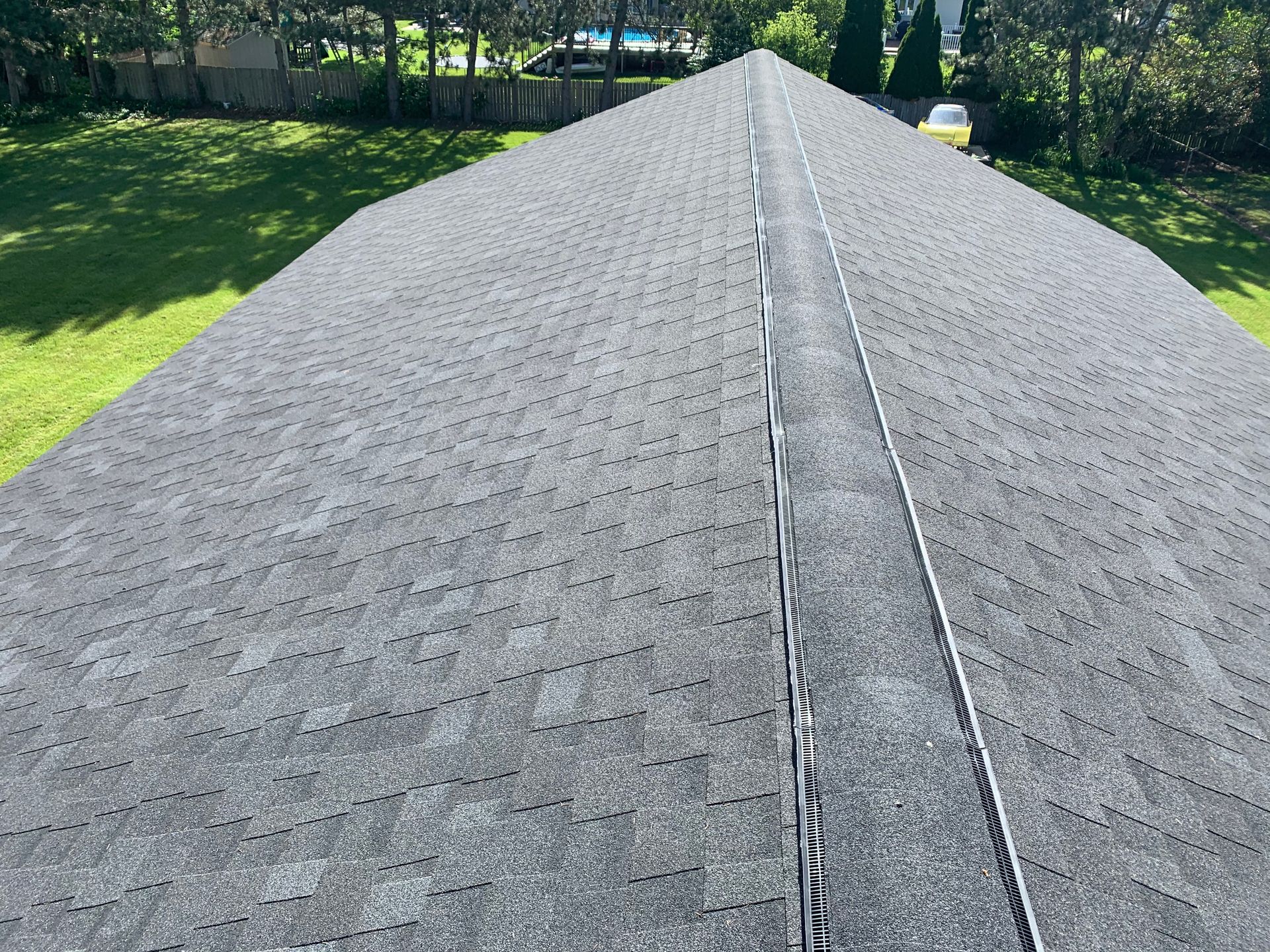 Gray shingled roof with a center ridge line, viewed from above against a green yard and trees
