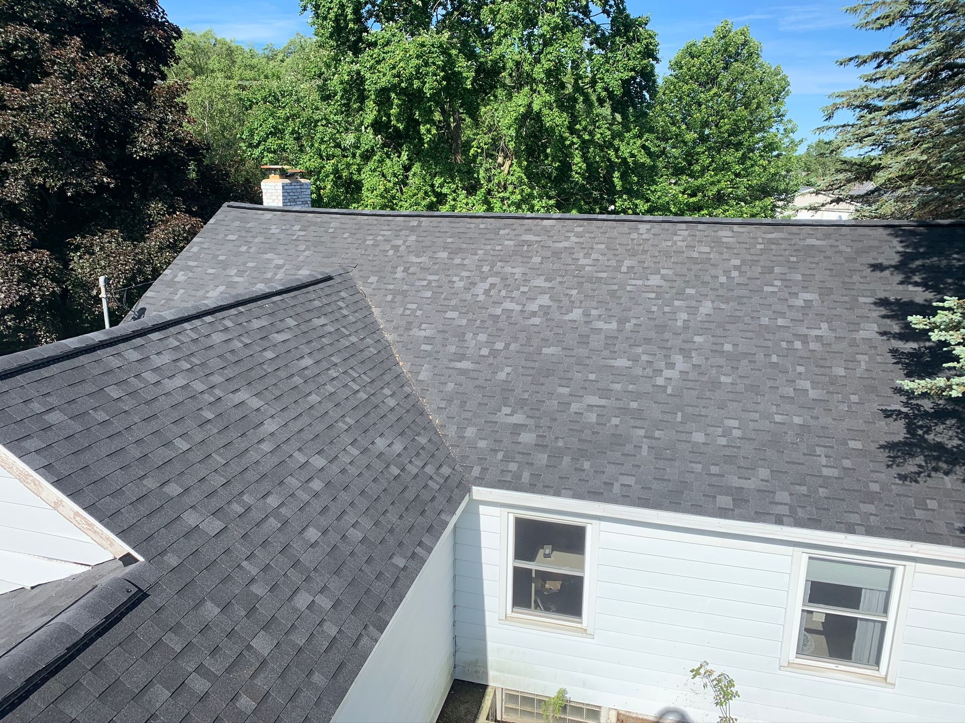 Gray shingled roof of a white house, viewed from above with trees in the background