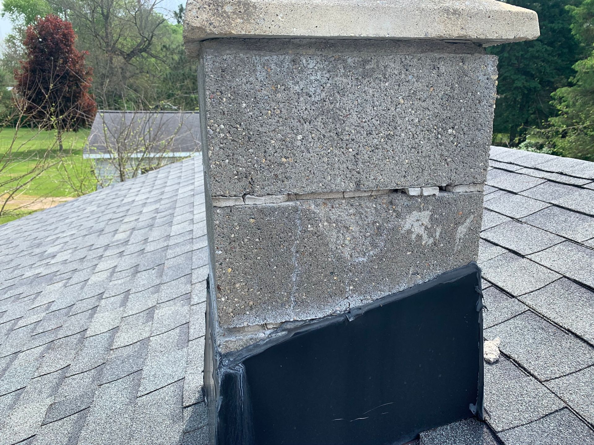 Stone chimney on a shingled roof with a dark metal flashing base.
