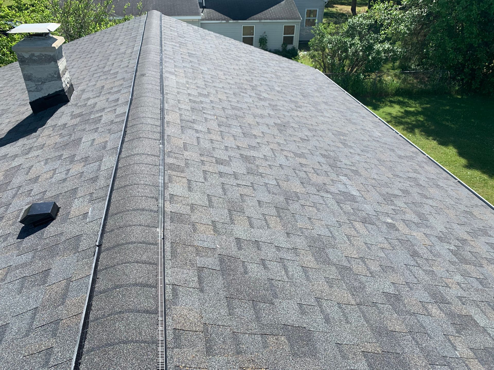 Gray shingled roof with a chimney and rooftop vent, viewed from above in daylight.