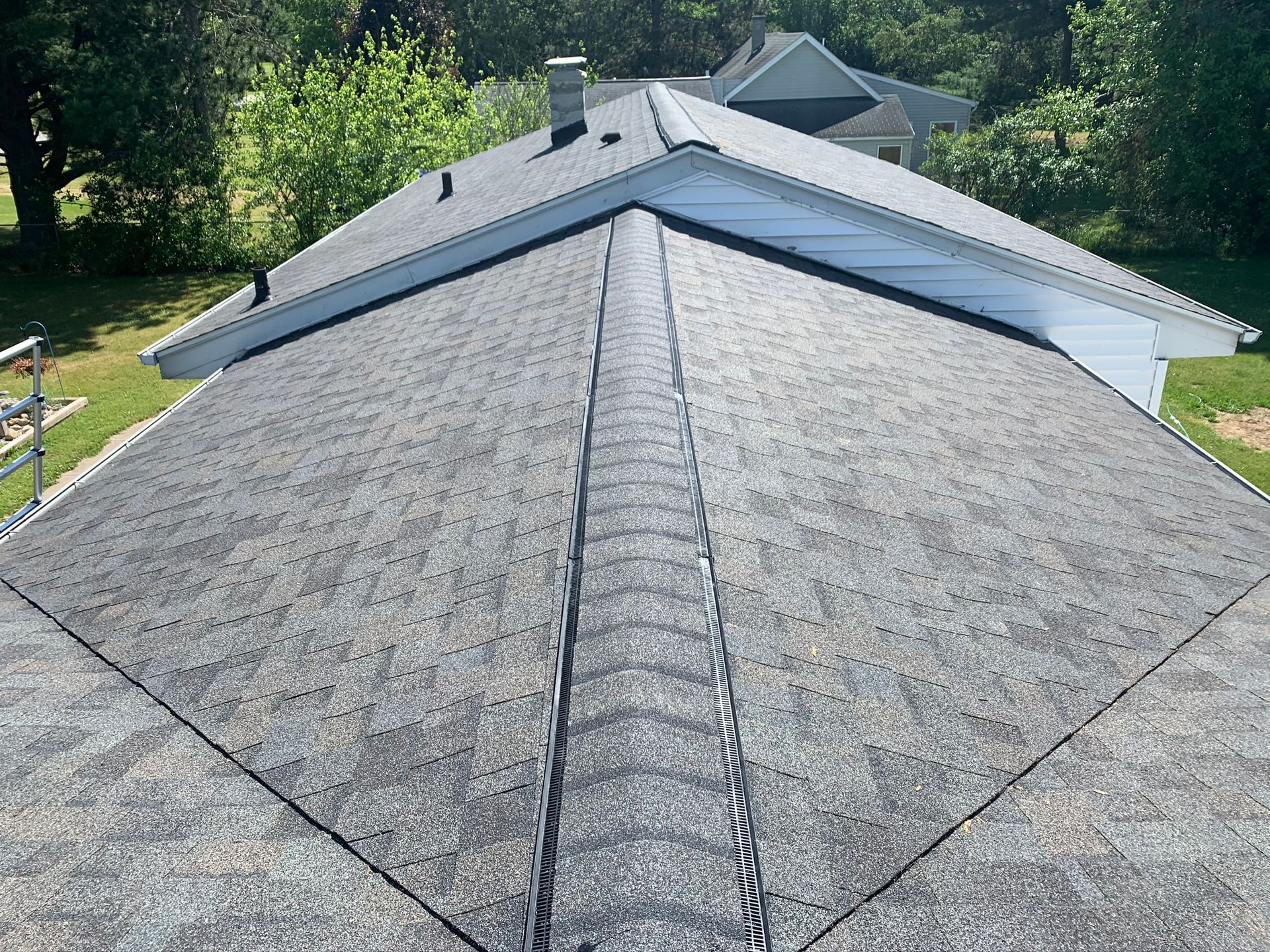 Gray shingled roof with a central ridge and dormer, viewed from above in a residential neighborhood