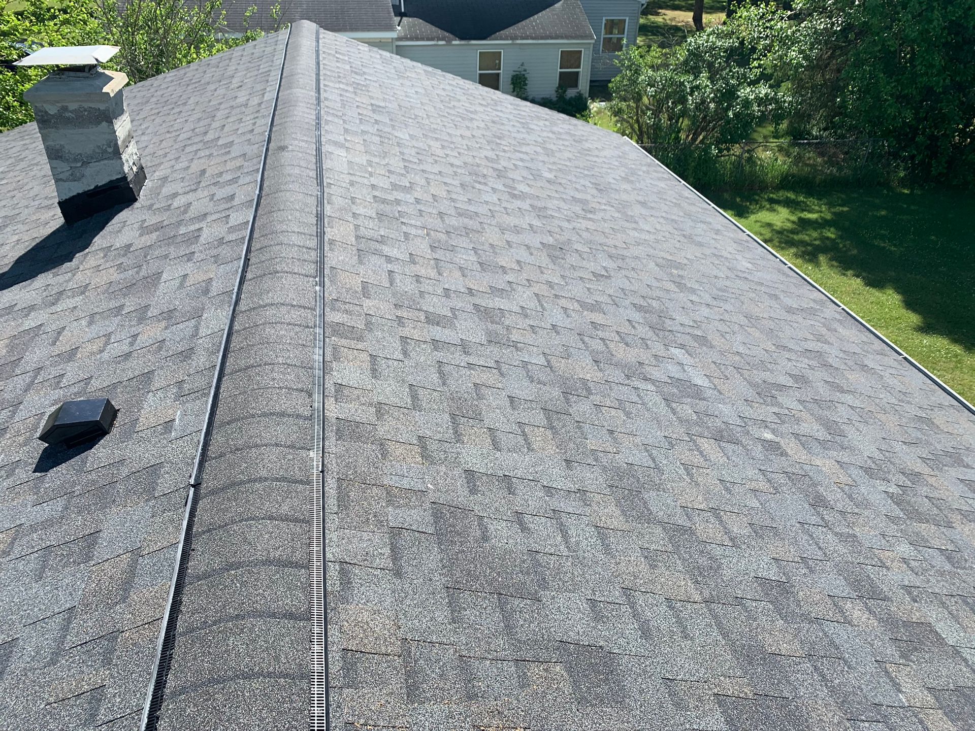 Rooftop covered in gray shingles with a ridge vent, seen from above on a sunny day
